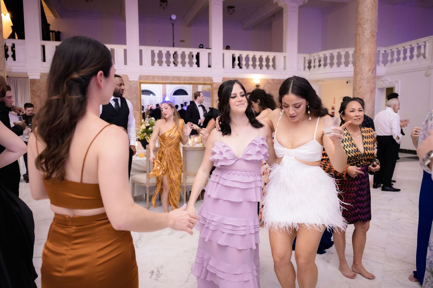 Wedding guests in colorful dresses dance and celebrate together on a grand ballroom floor.