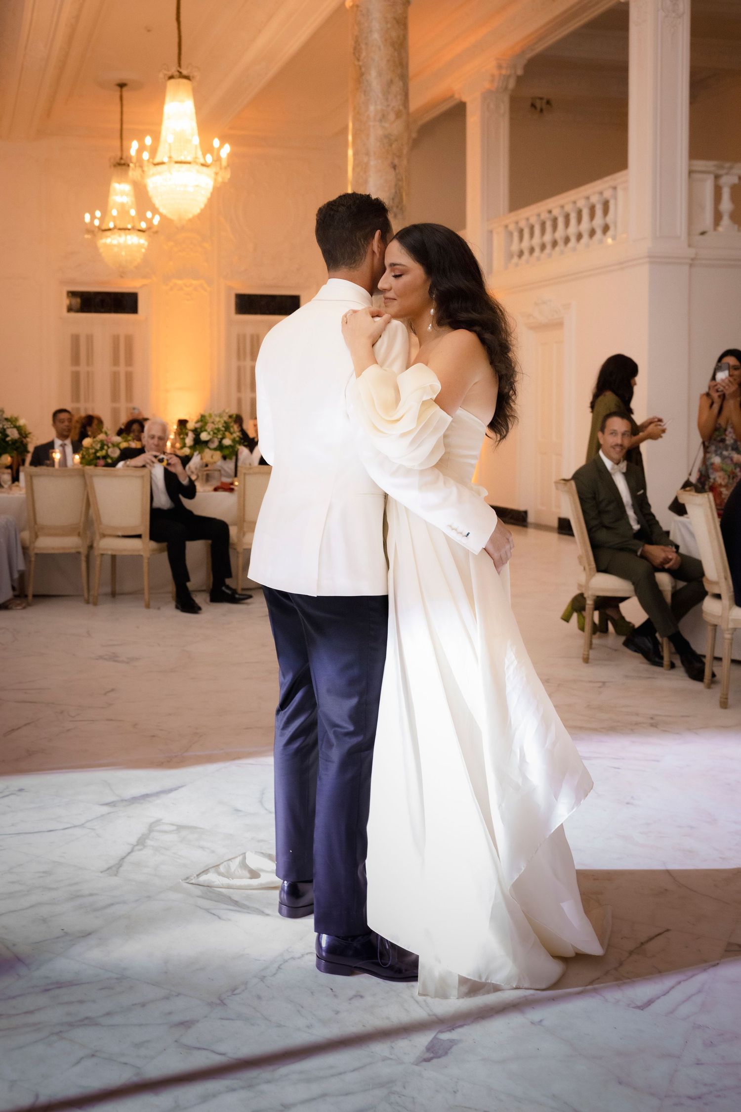 First dance at wedding reception in elegant ballroom with chandeliers.