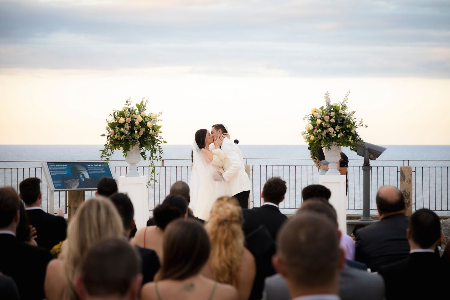 Wedding ceremony silhouetted against a serene oceanfront backdrop at dusk.