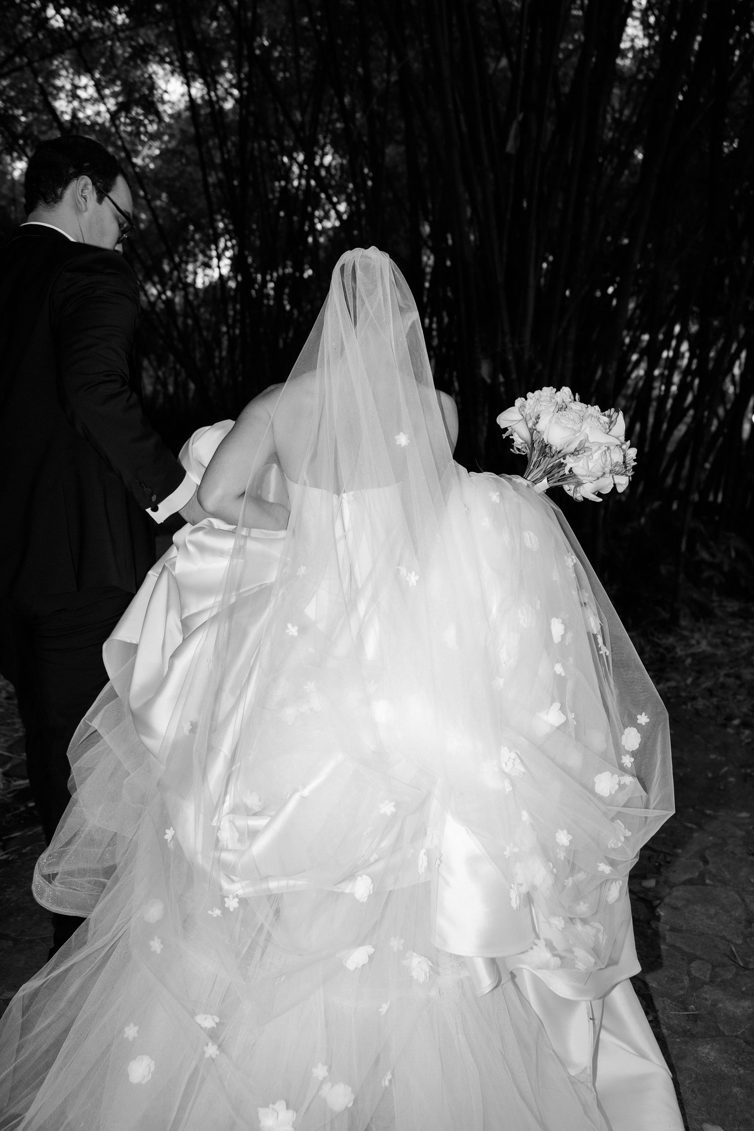 A flowing white wedding dress with ruffled layers and tulle fabric photographed in a wooded outdoor setting.