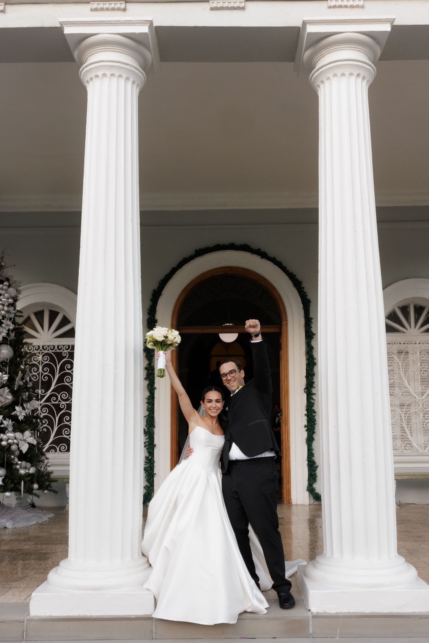 Newlyweds celebrate between classic white columns at venue entrance.