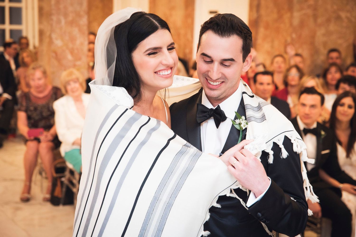 Elegant wedding ceremony inside a luxurious ballroom decorated with floral arrangements and classic architectural details.