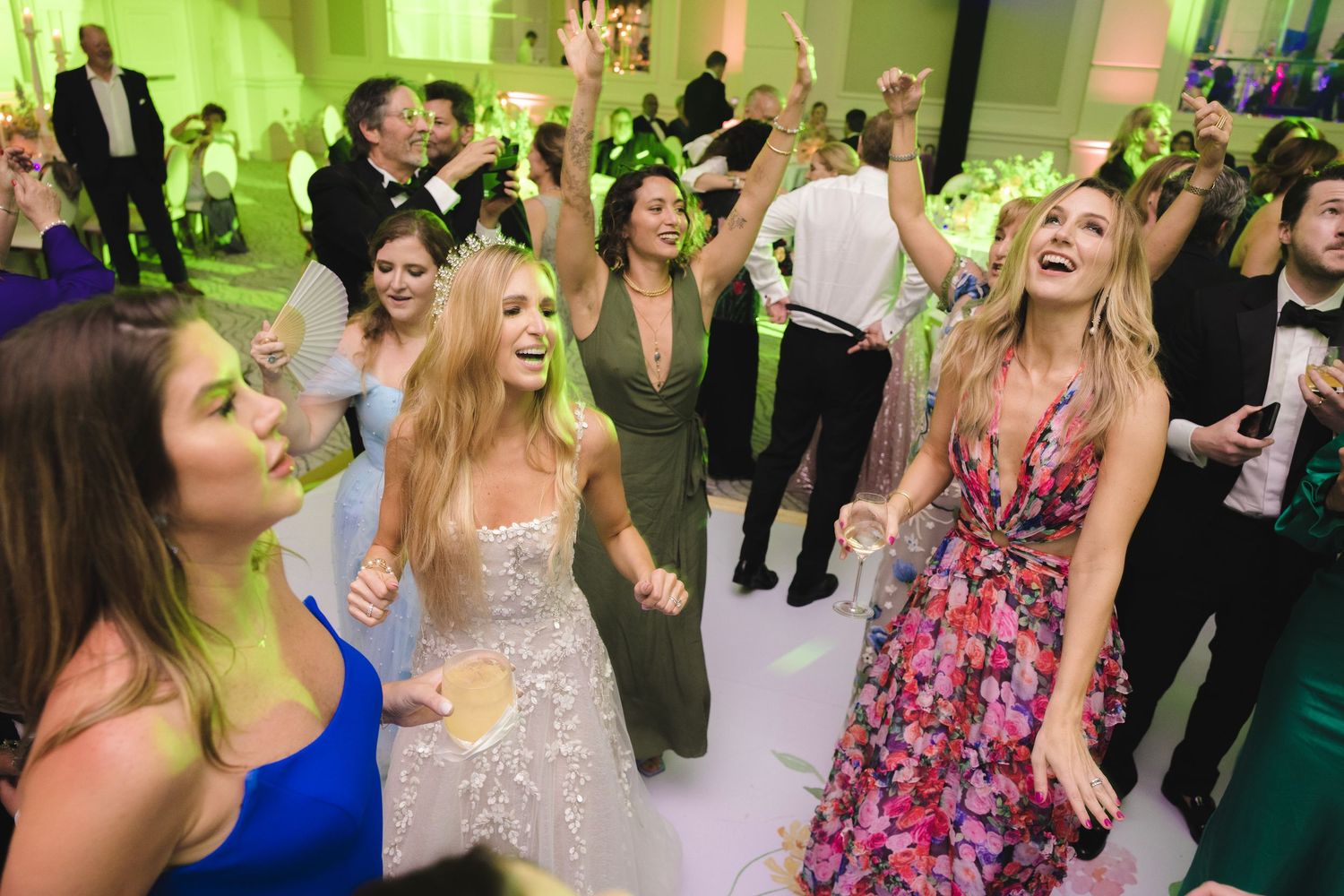 Wedding guests dance together on the reception dance floor under bright green lighting.