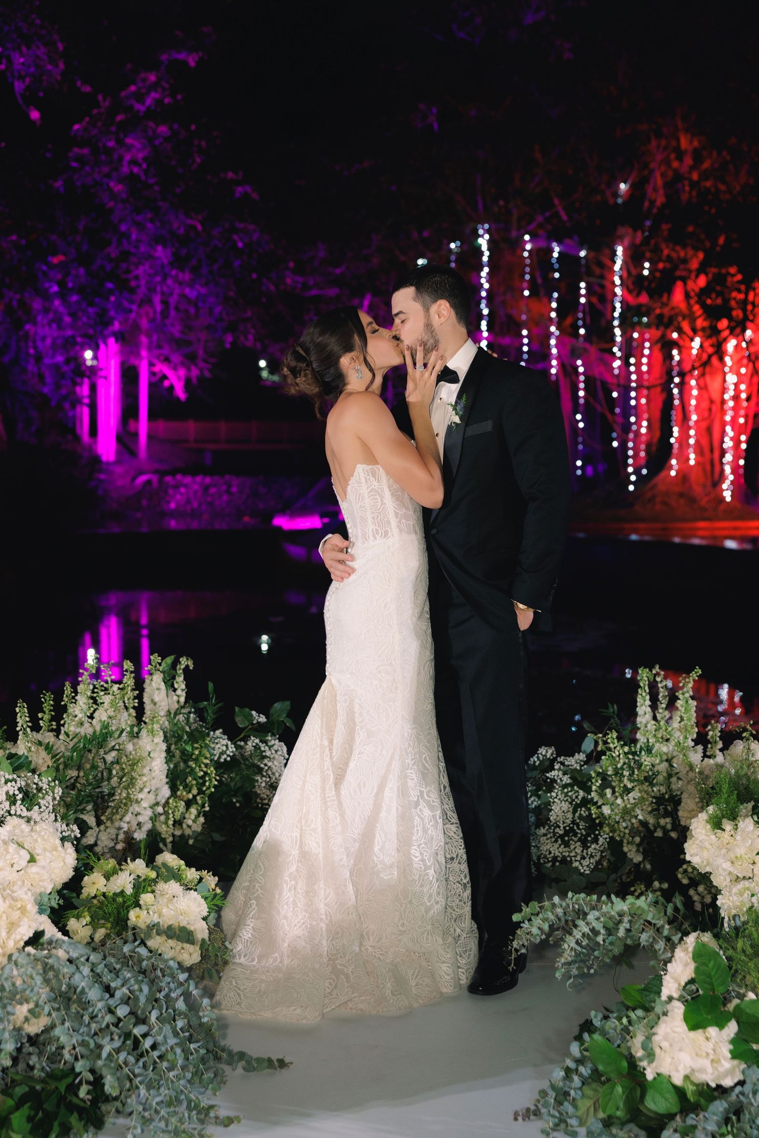 An intimate wedding portrait at night with dramatic purple lighting and white floral decorations.