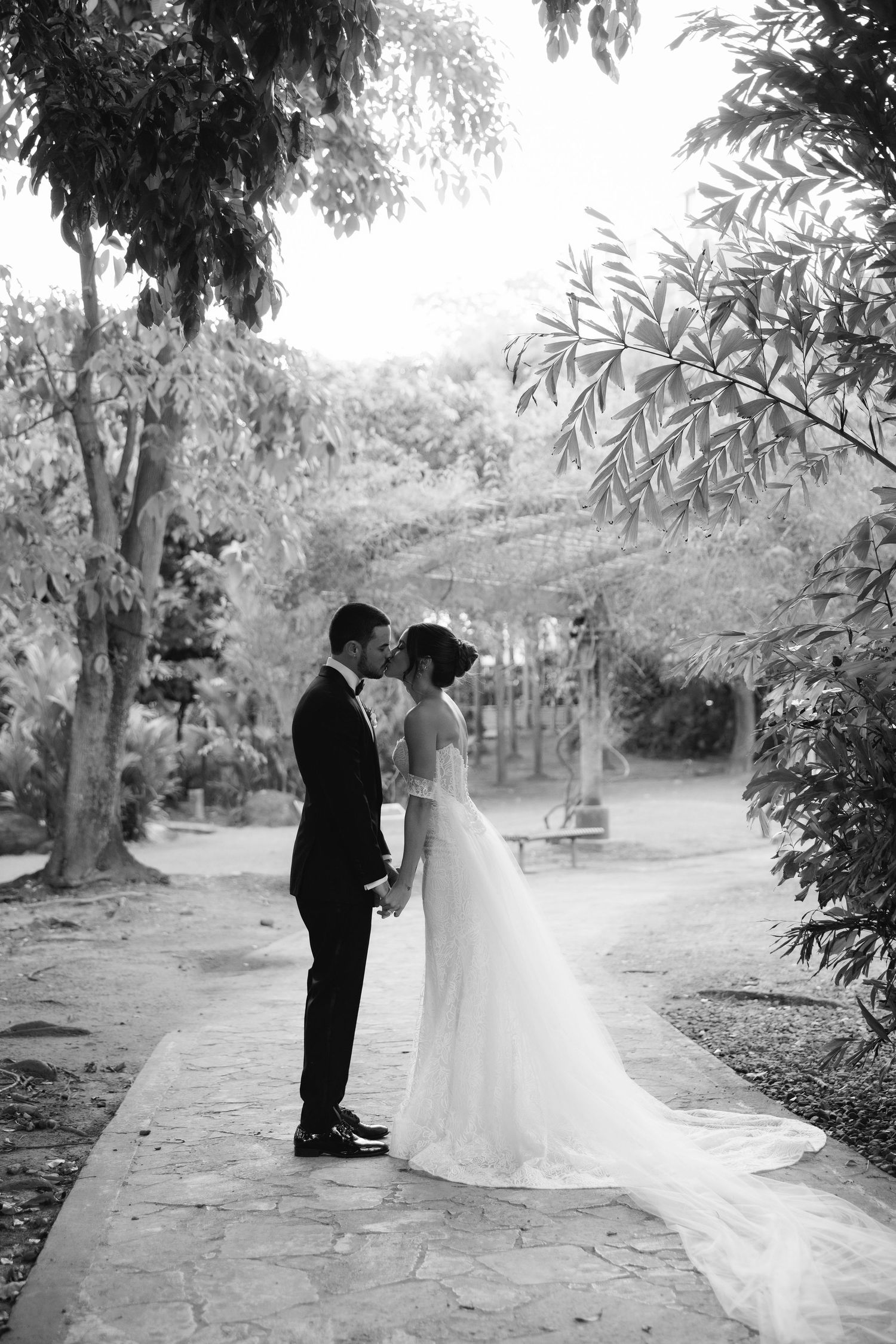 A charming black and white wedding photo series of a couple in a romantic garden setting with overhanging trees.