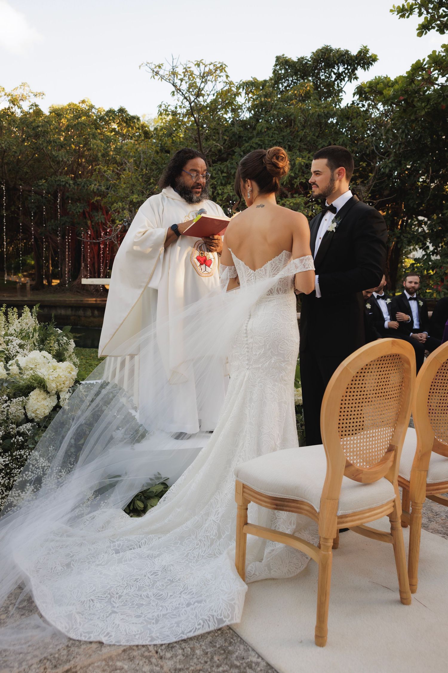 Elegant wedding setting with flowing white dress train and wicker chairs on outdoor terrace.