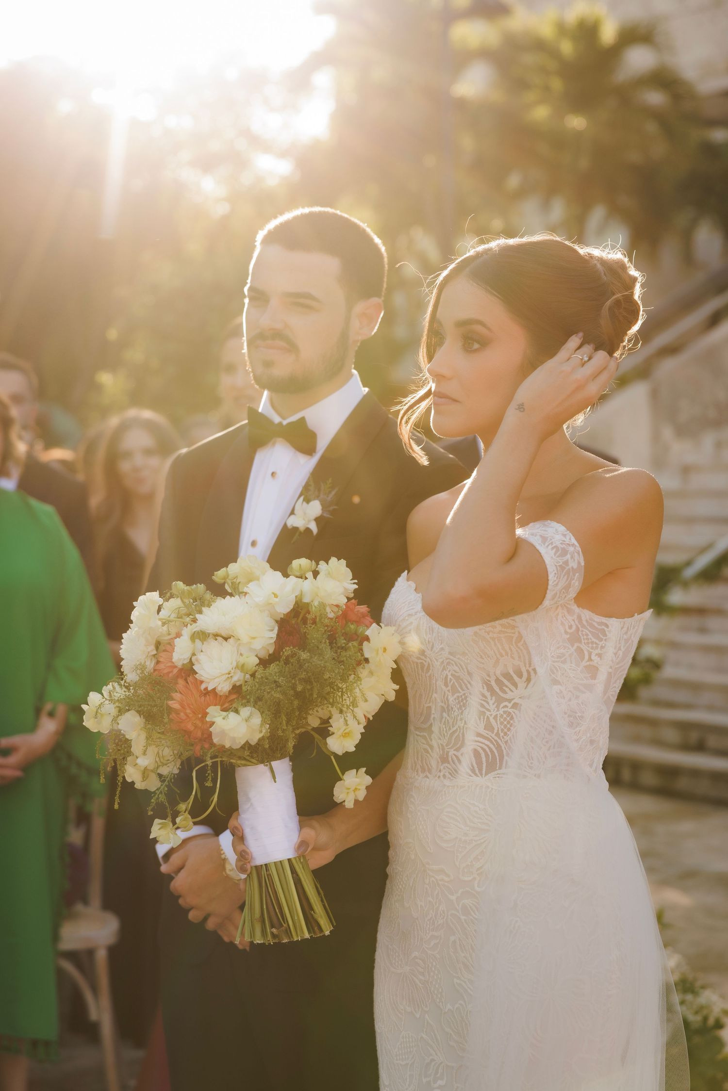 A beautiful outdoor wedding ceremony at sunset with lace dress details and white floral bouquet.