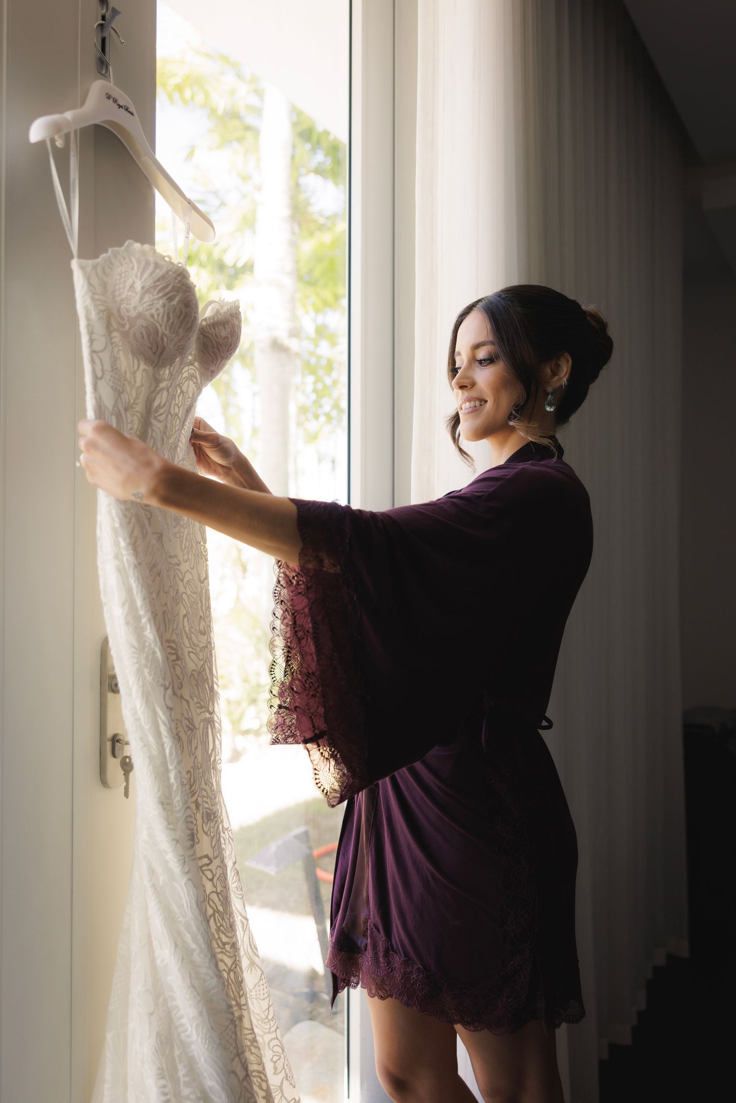 Wedding dress being admired near a window in natural light with elegant lace details.
