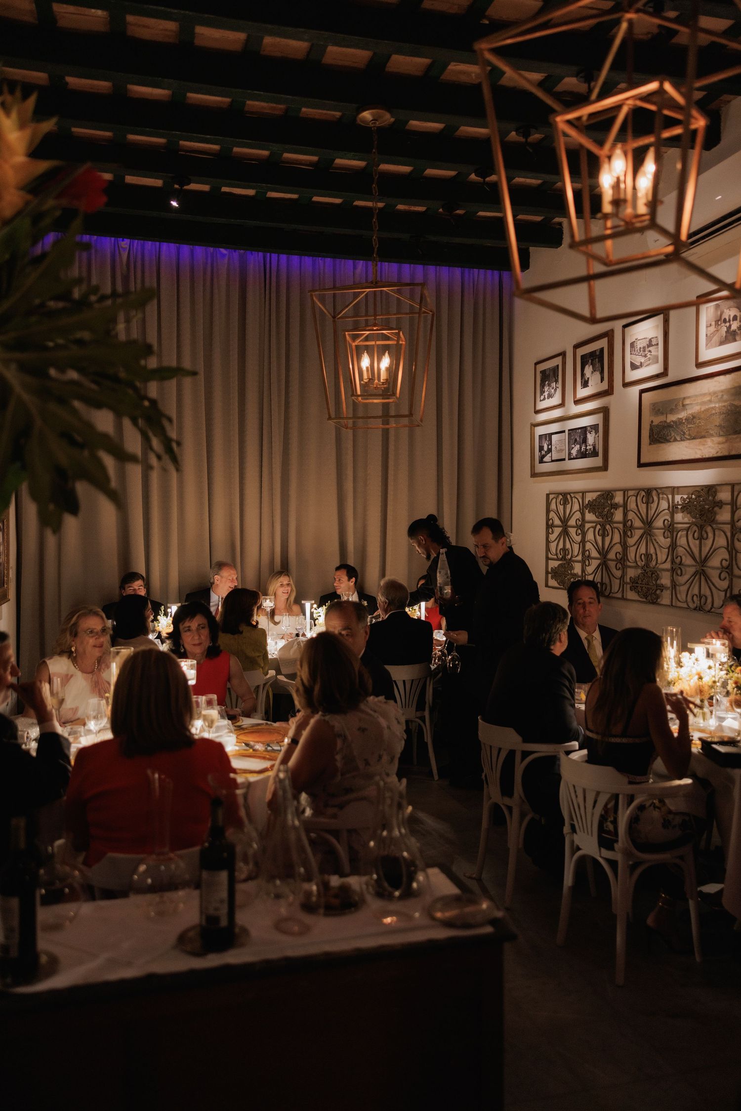 Guests dining in a dimly lit upscale restaurant interior with moody lighting, copper accents and gallery wall decor.