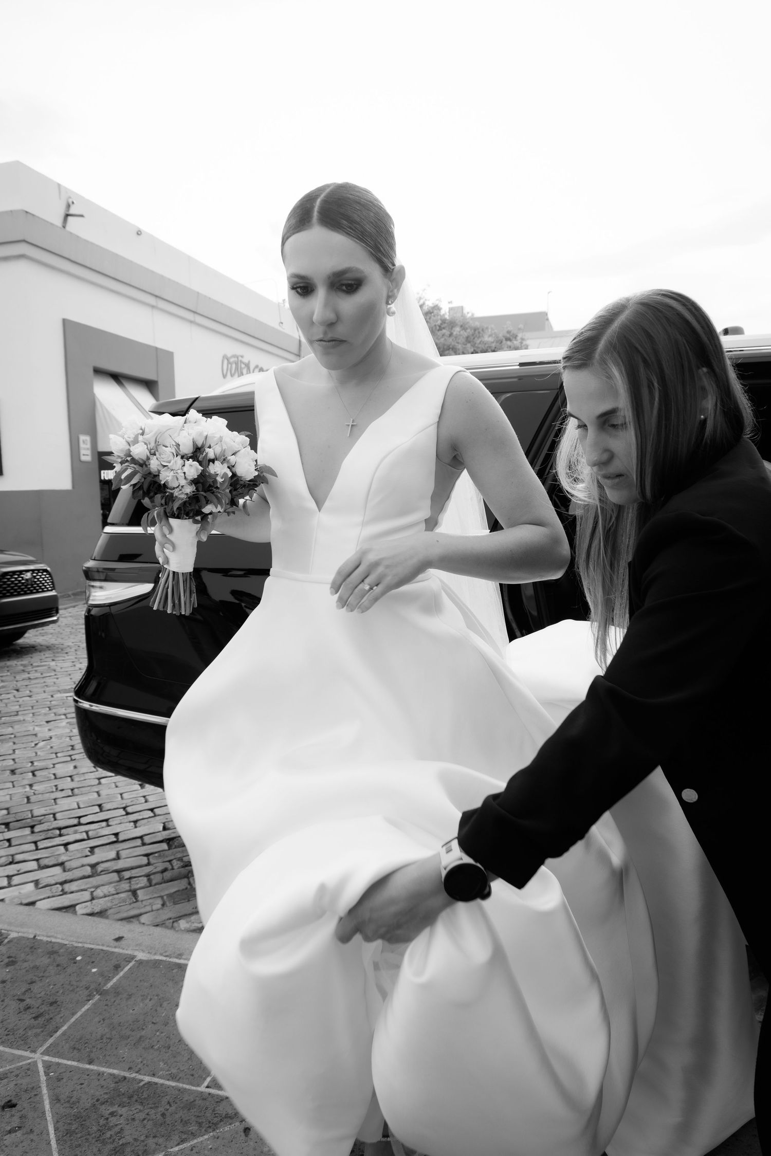 Wedding dress preparations showing assistants adjusting the white gown outdoors.