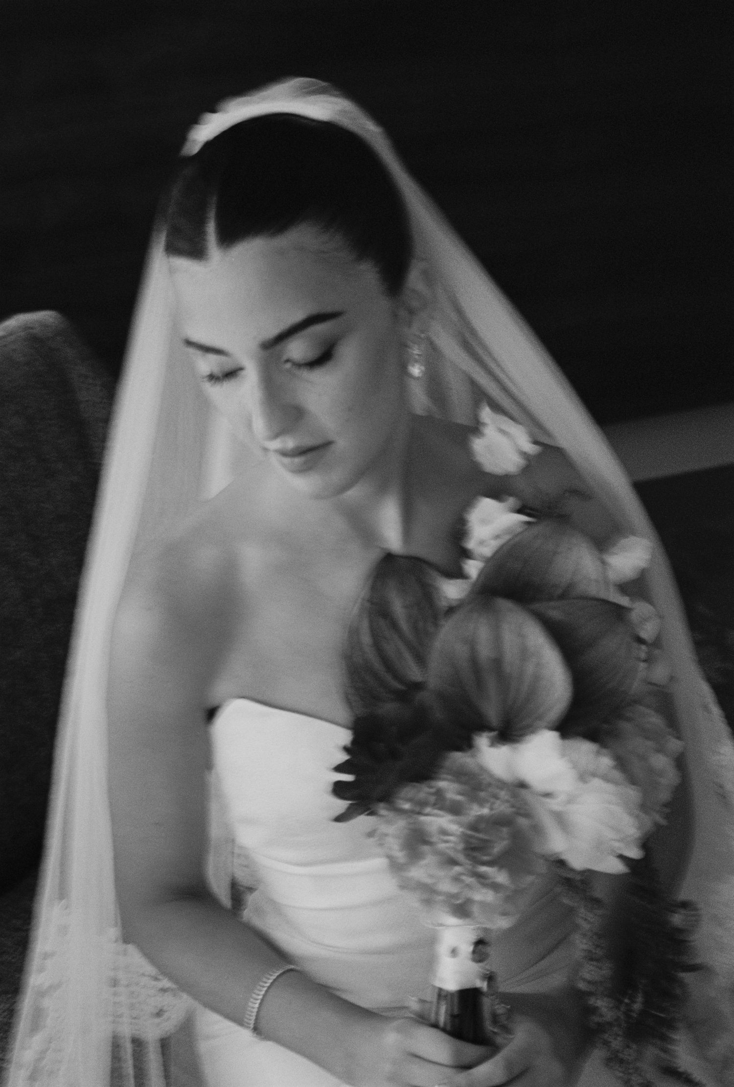 Black and white photo of a bride in a strapless gown and veil holding a floral bouquet.
