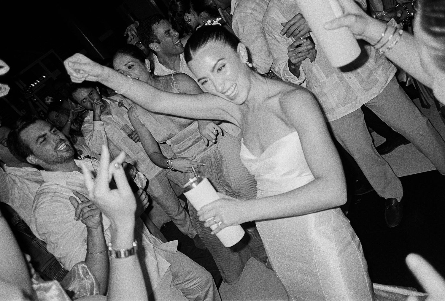 Woman in white dress dancing energetically at a crowded black and white party event.