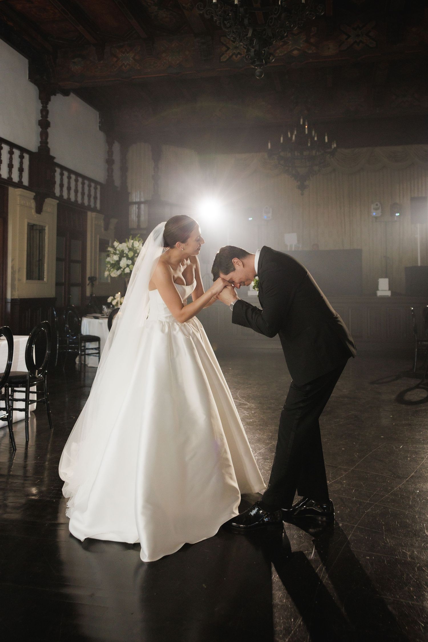 Dramatic silhouettes of a wedding dress being adjusted in a dark room with streaming light.