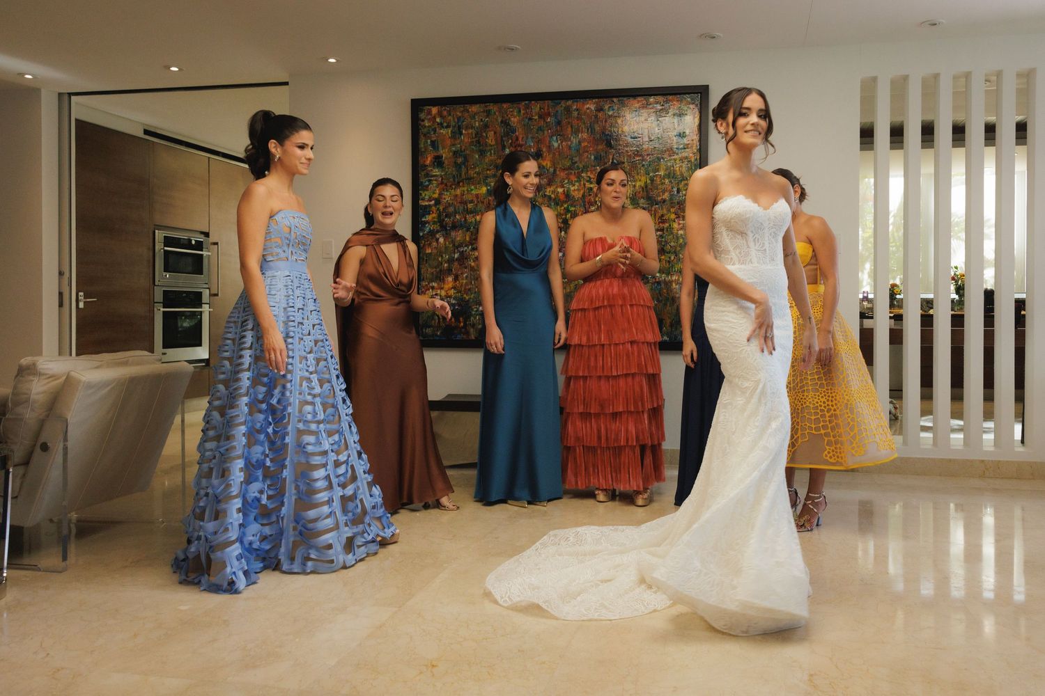 Wedding party poses in a modern indoor space with bridesmaids in vibrant dresses and a bride in white.