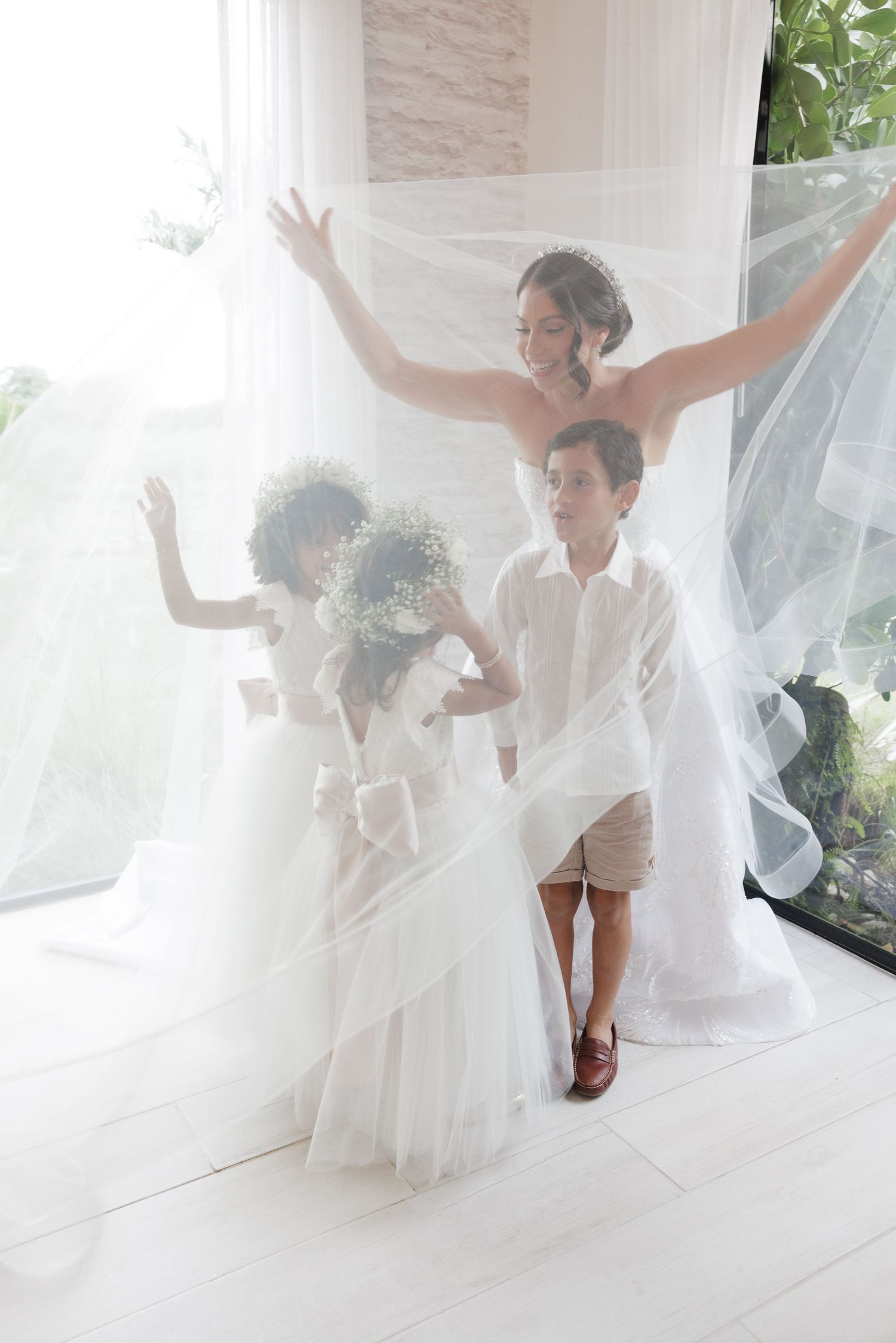 A playful wedding moment captured with flowing white dresses and raised arms in celebration.