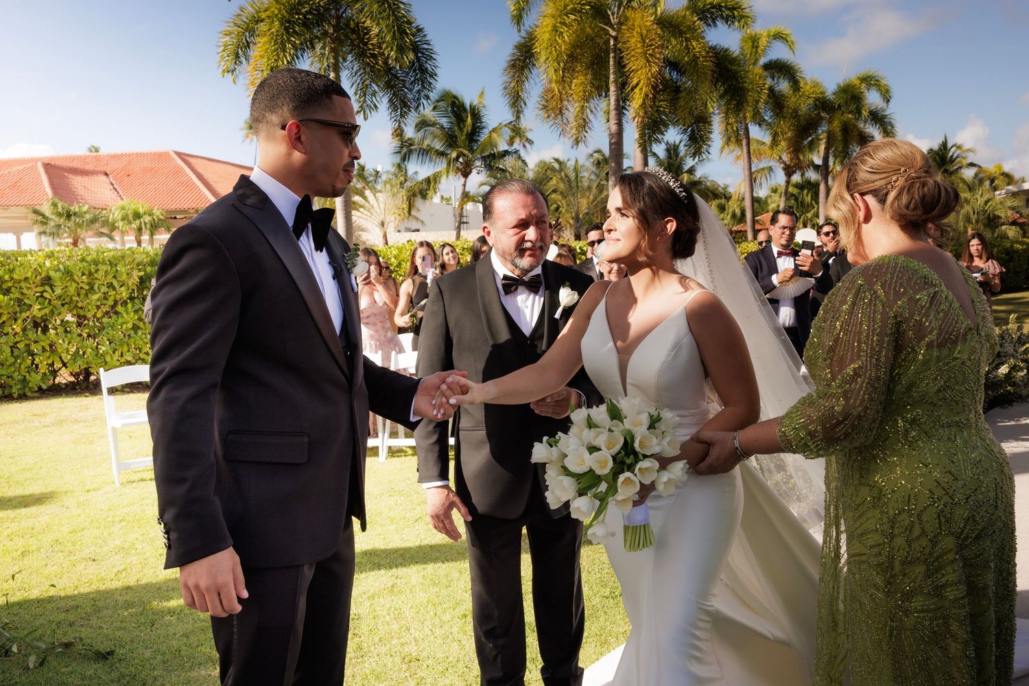 Guests mingle and celebrate during an outdoor wedding reception at a tropical venue with palm trees in the background.