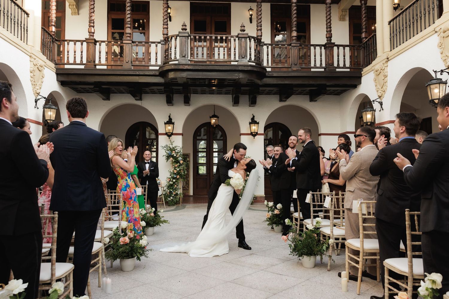 A romantic courtyard wedding ceremony surrounded by Spanish colonial architecture and decorative floral arrangements.