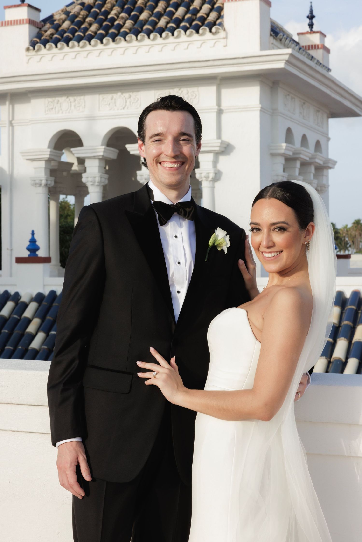 Classic wedding photo shoot in front of ornate white stone architecture with Spanish tiled roof.