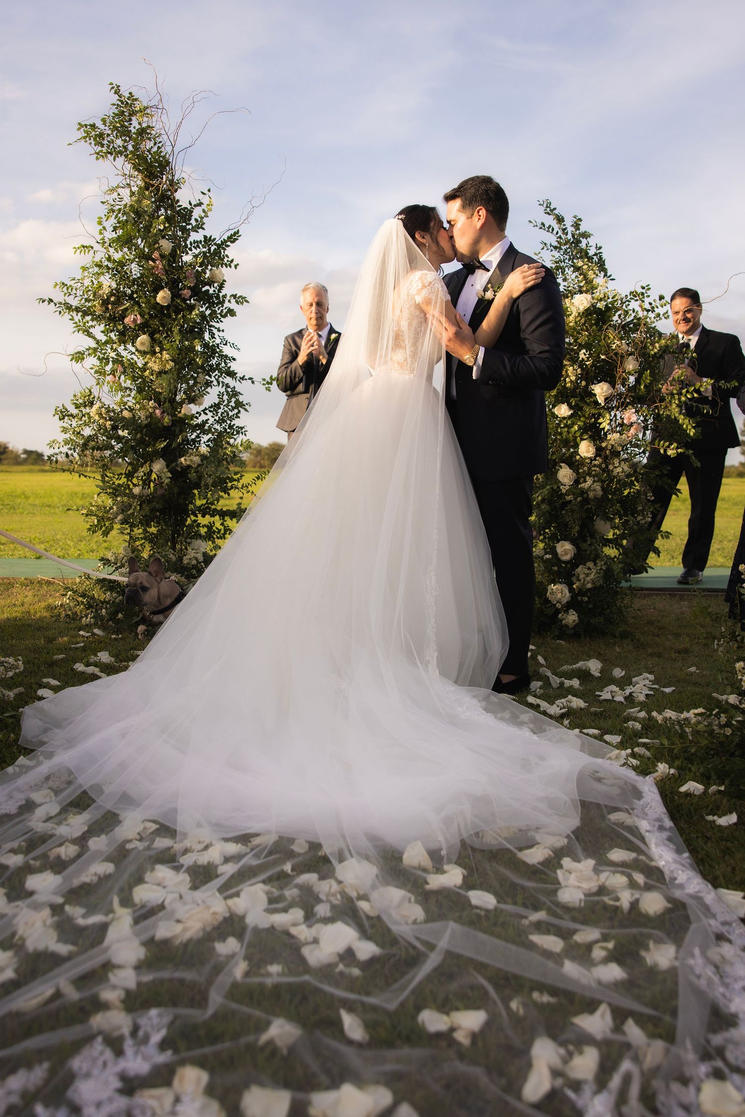 A wedding couple embracing during sunset with flower petals scattered around the flowing white dress.