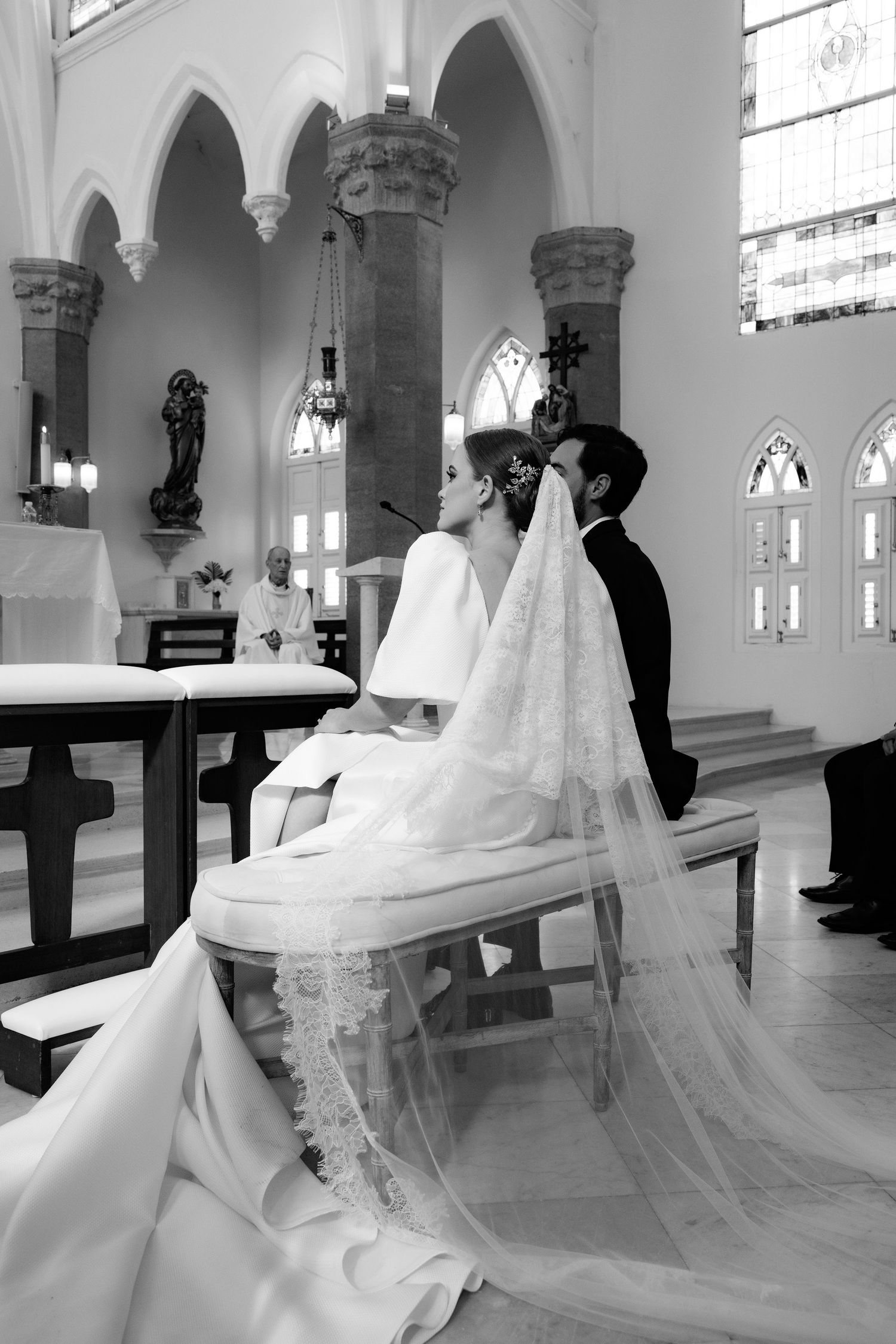 Beautiful black and white wedding ceremony photo in a traditional church with ornate stone columns and stained glass windows.