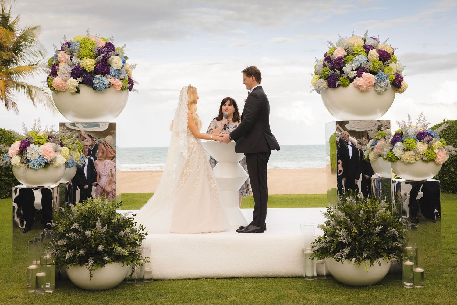 Floral wedding ceremony setup on a white platform overlooking the ocean with elegant flower arrangements.