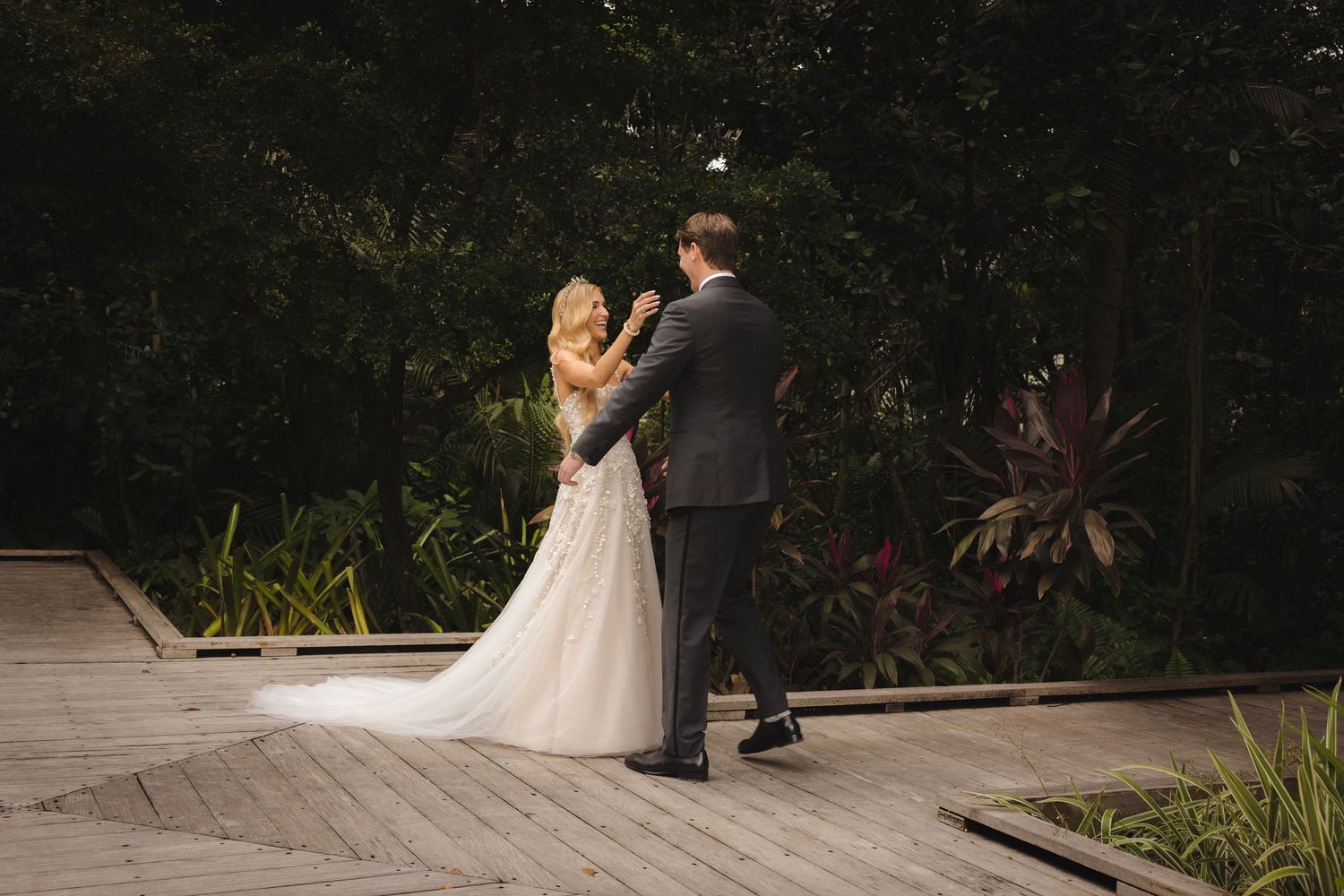 Wedding couple holds hands and kisses during an intimate garden ceremony surrounded by lush greenery.