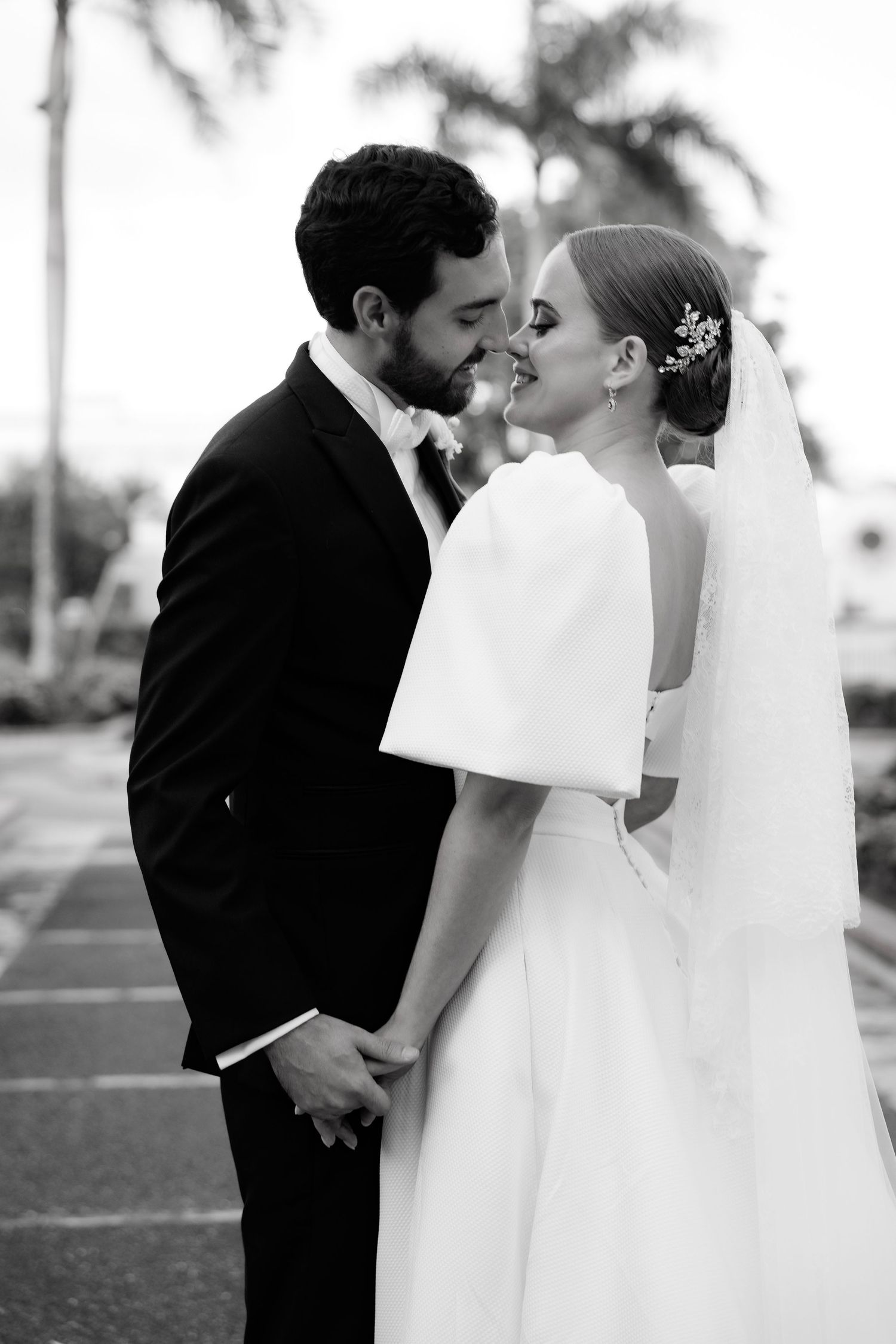 Black and white wedding photo capturing a romantic moment between a couple in elegant wedding attire.