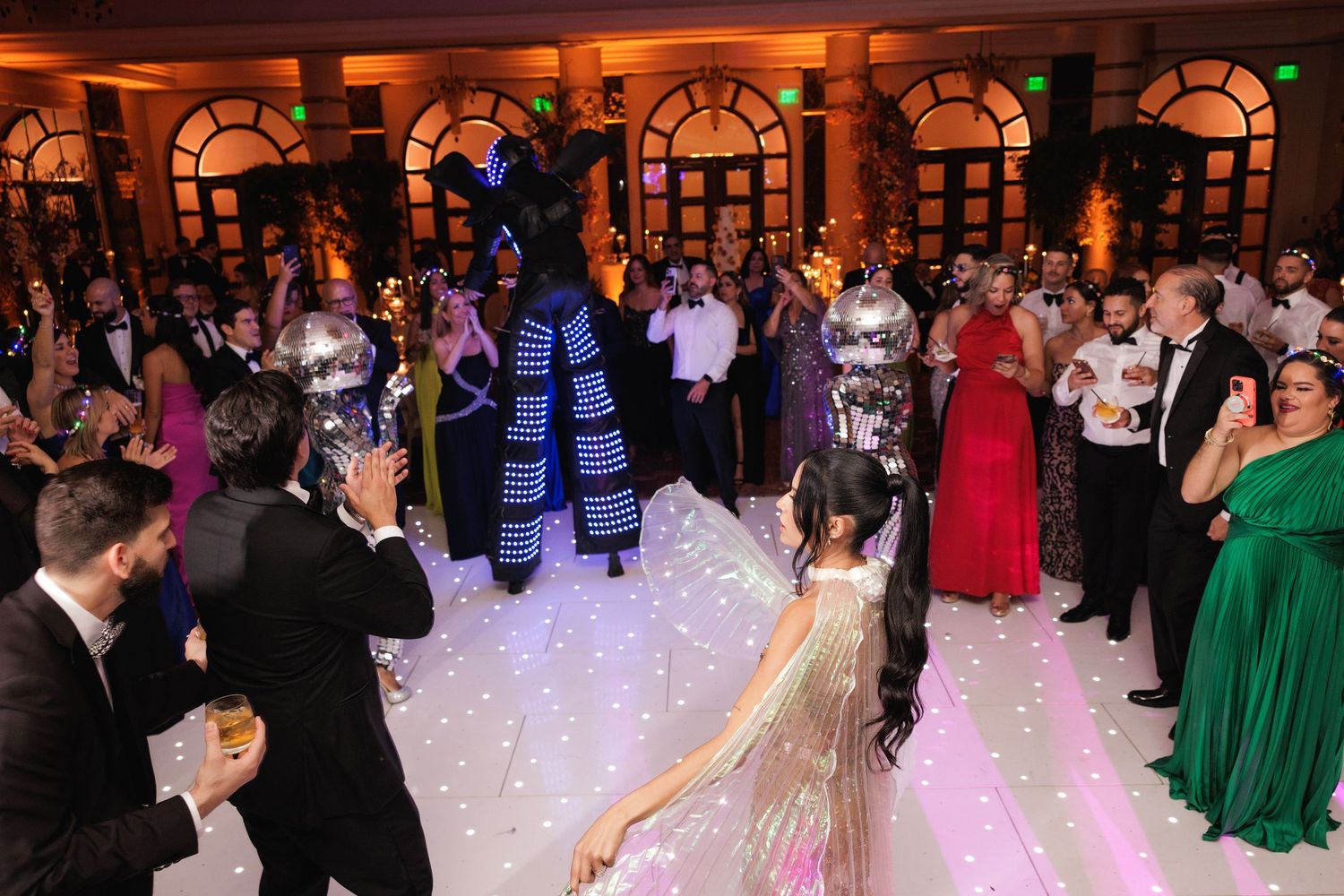 A large wedding reception dance floor filled with guests celebrating and dancing under elegant lighting.