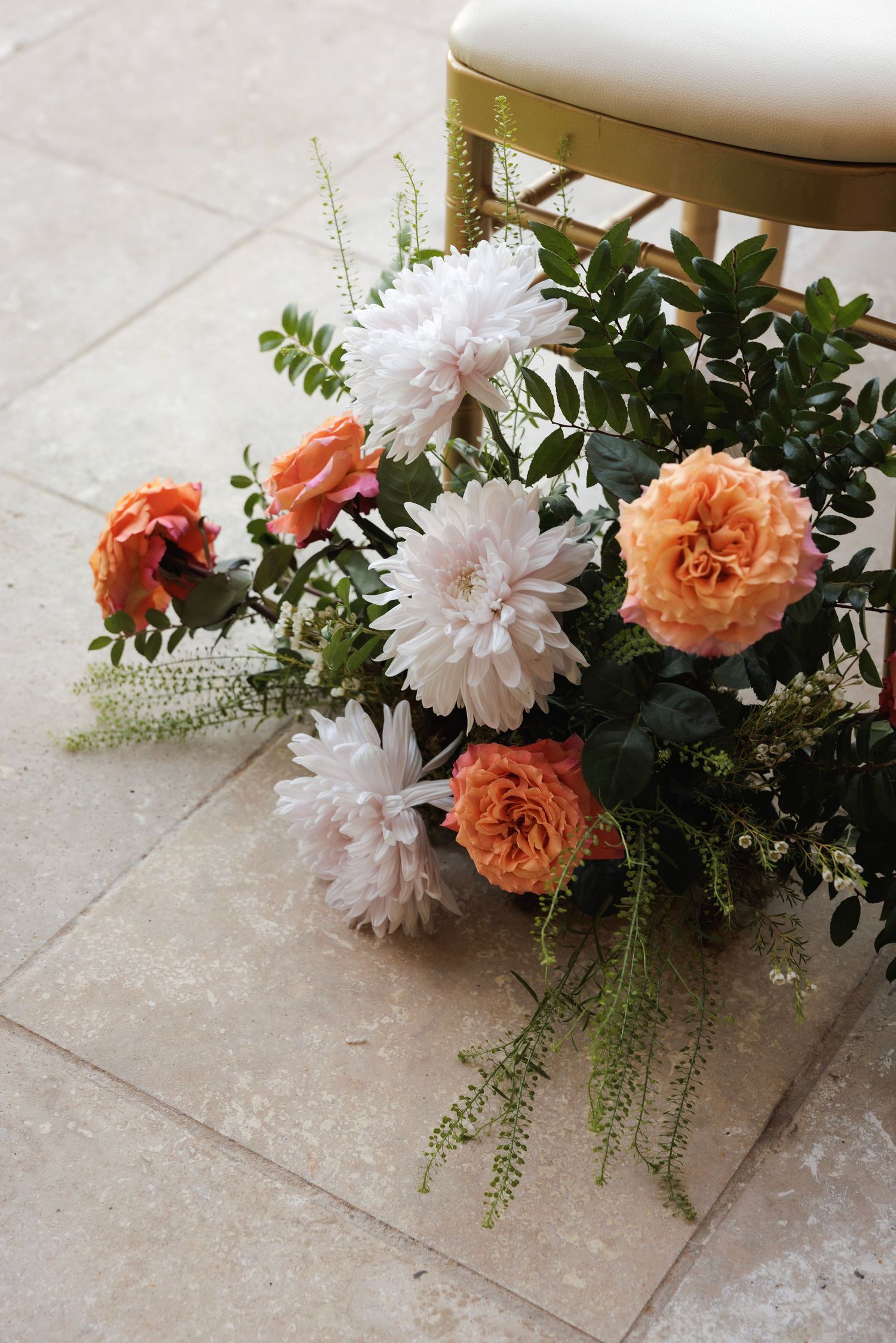 Floral arrangement with coral roses and white dahlias against neutral tile flooring.