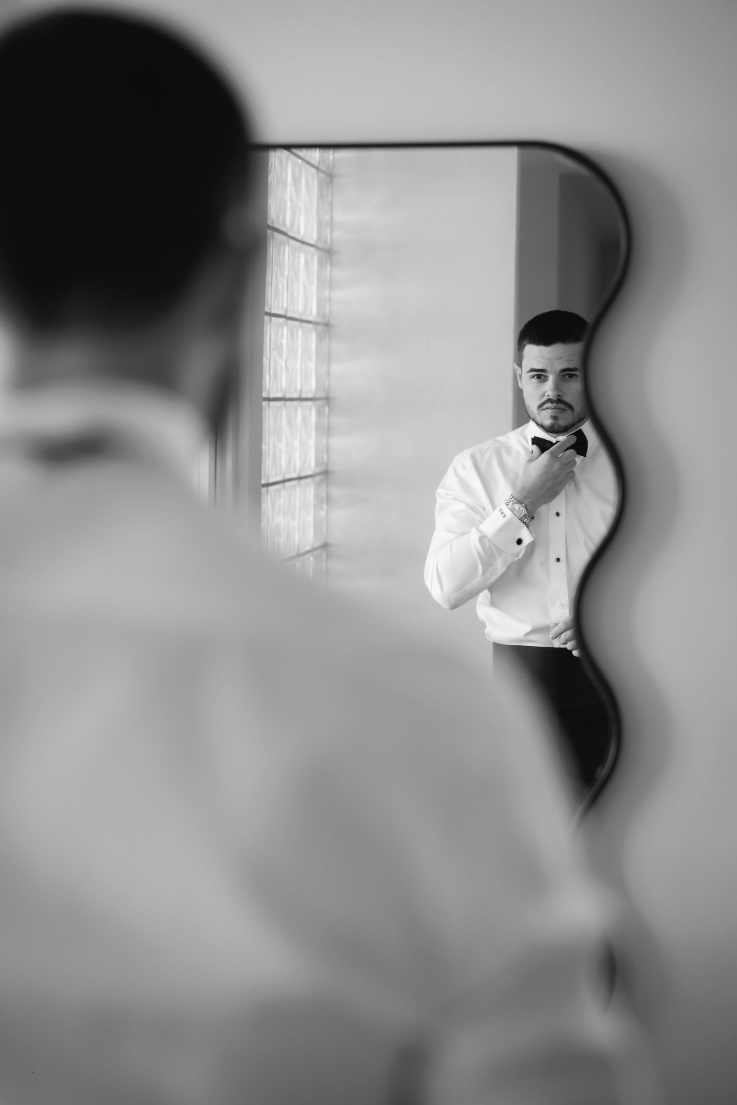 Black and white sequence of groom adjusting his bowtie in mirror reflection.