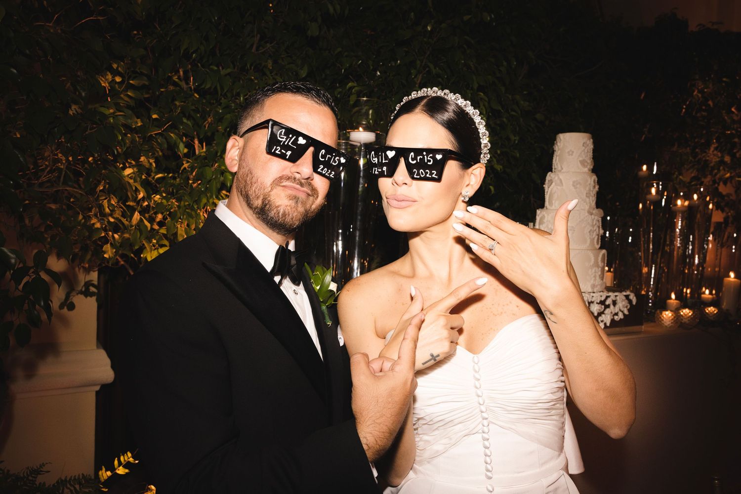 A couple wearing matching pixelated sunglasses poses together at a wedding reception celebration.