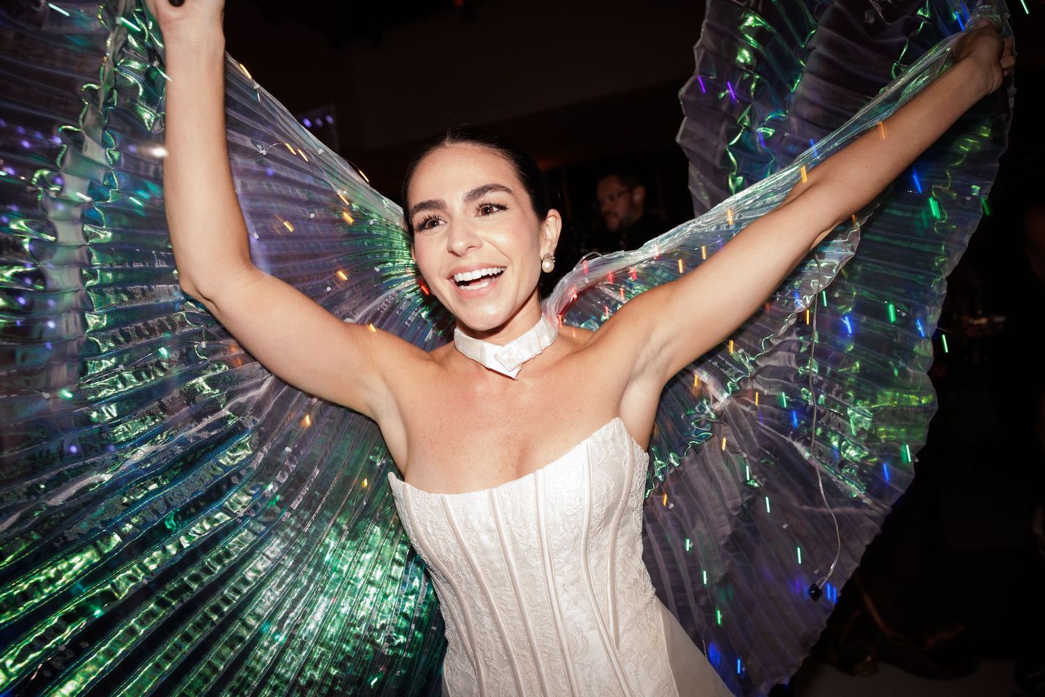 Bride wearing strapless gown with iridescent butterfly wings celebrates on the dance floor.