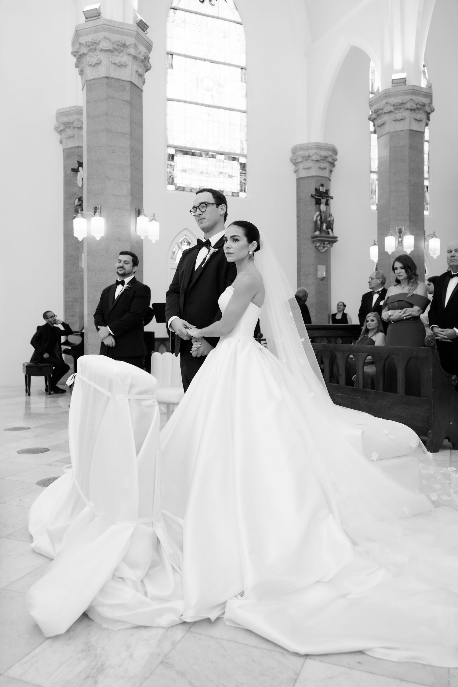 A wedding ceremony takes place in a grand church with ornate stone pillars and marble floors.