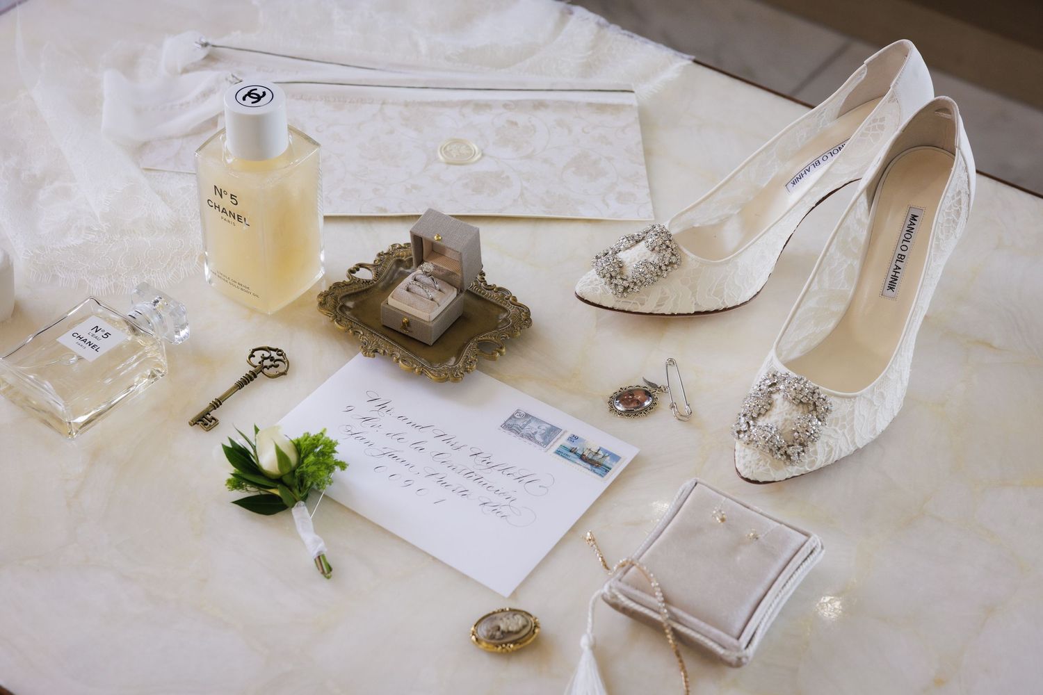 Wedding detail shot of accessories including shoes, jewelry and invitation on white tablecloth.