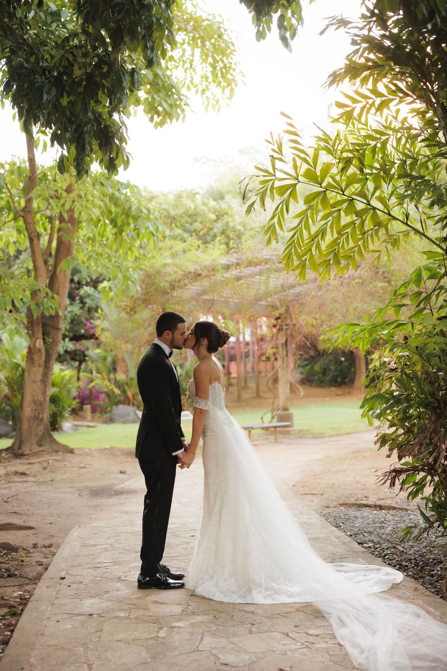 Wedding couple walking along a garden path surrounded by lush greenery.