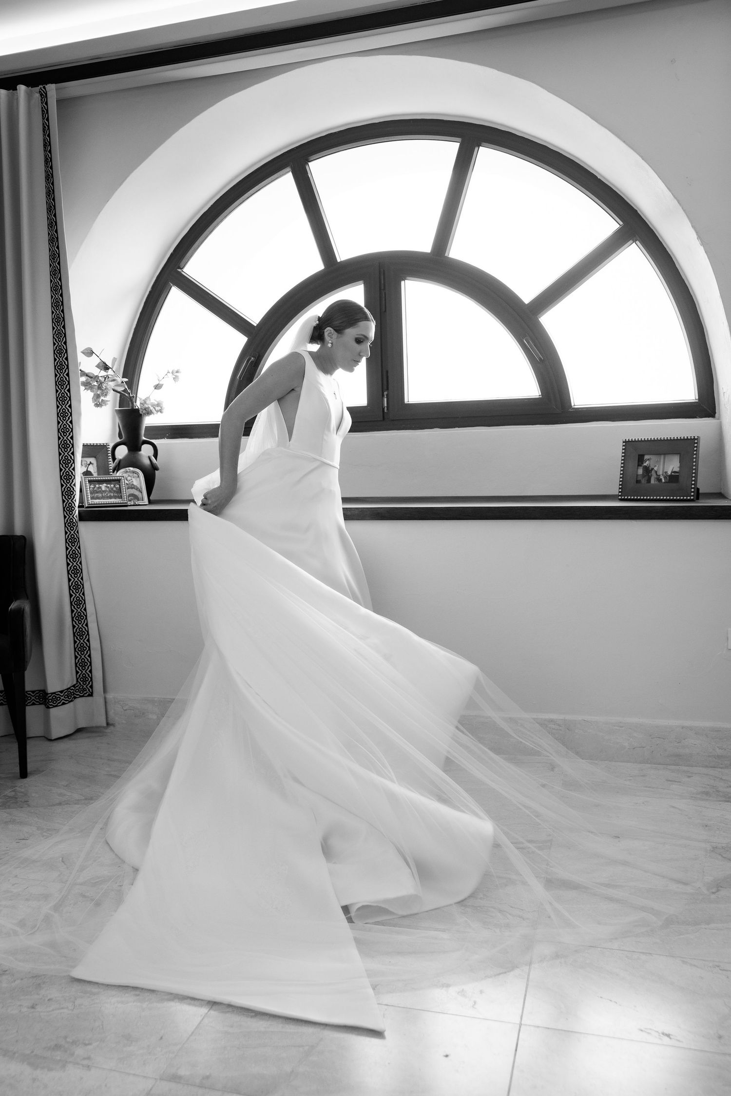 Black and white photos showing flowing white wedding dress veil twirling gracefully in an arched window room.
