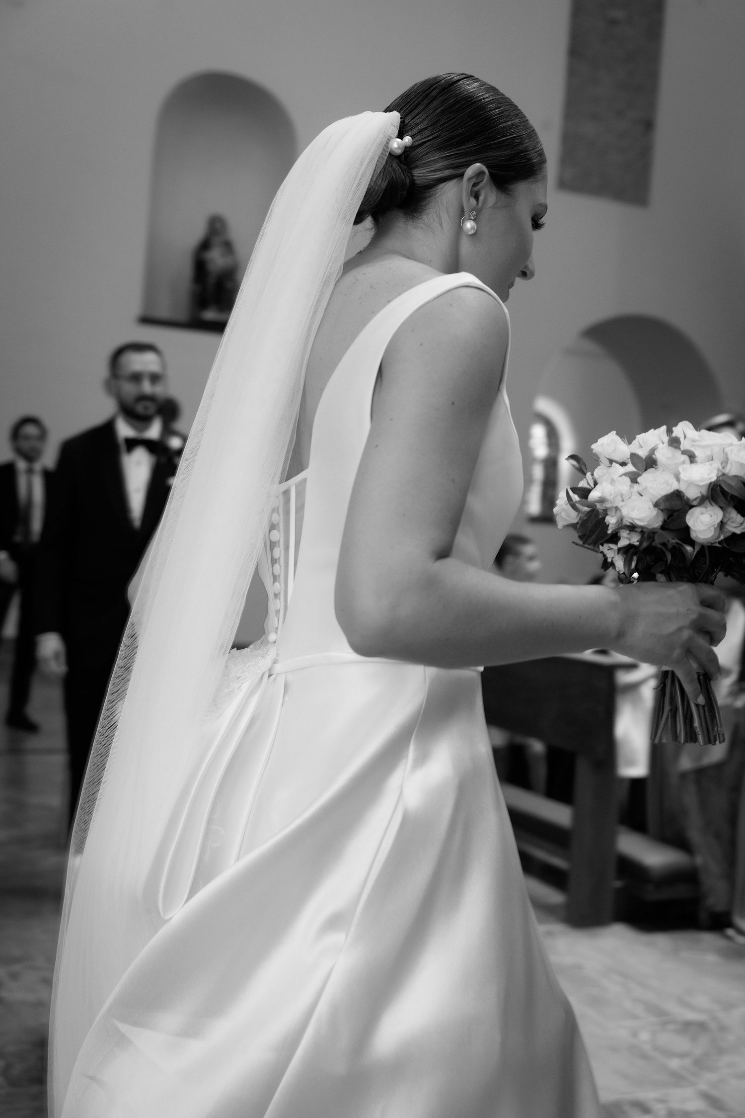 Classic black and white wedding photo showing elegant bride in sleeveless gown holding bouquet in church.
