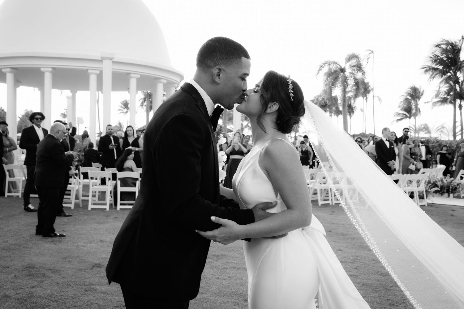 Couple shares romantic dance outdoors at sunset during their wedding celebration at beachfront venue.
