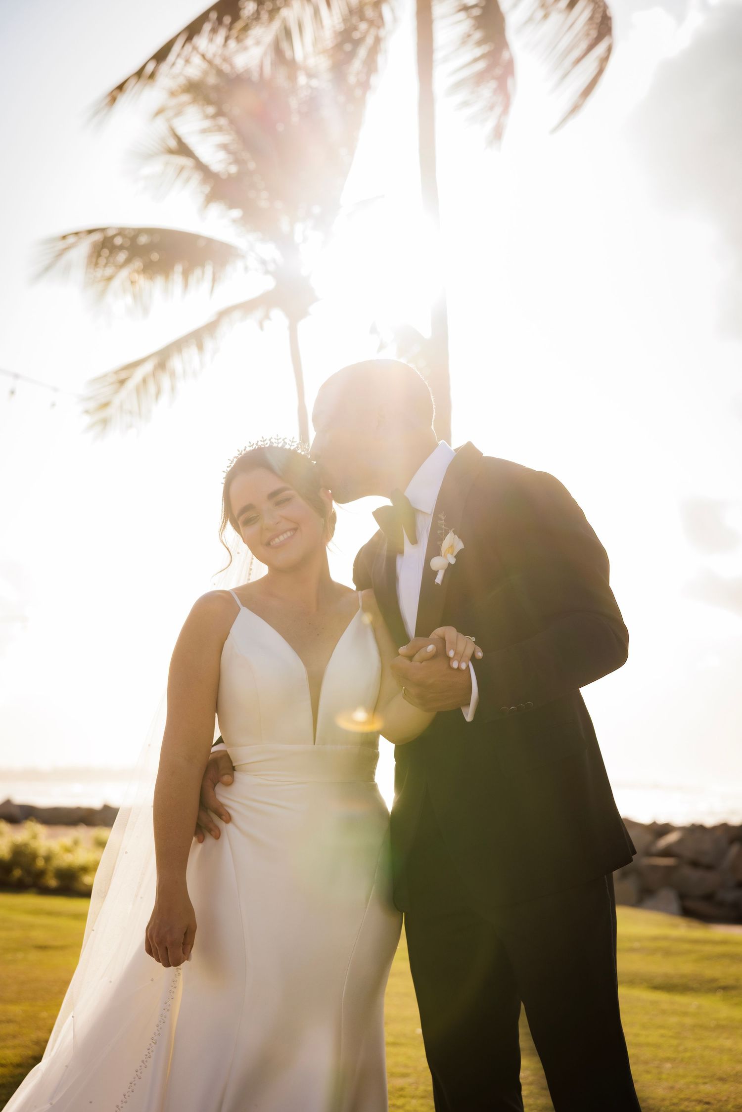 Sun flares beautifully through palm trees as couple shares intimate moments during outdoor wedding photo session.