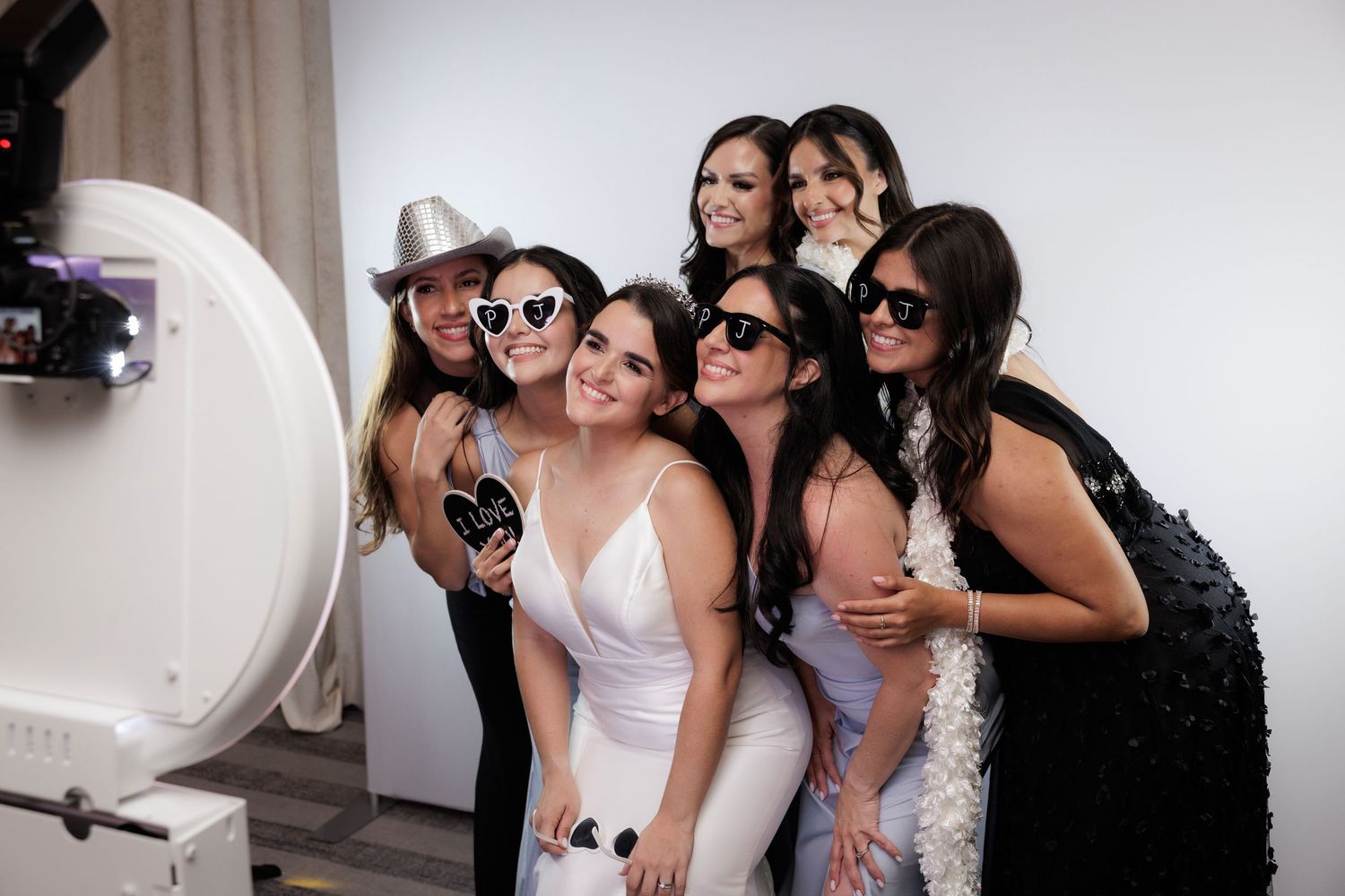 A group of friends wearing sunglasses pose and laugh together while taking selfies at a joyful gathering.