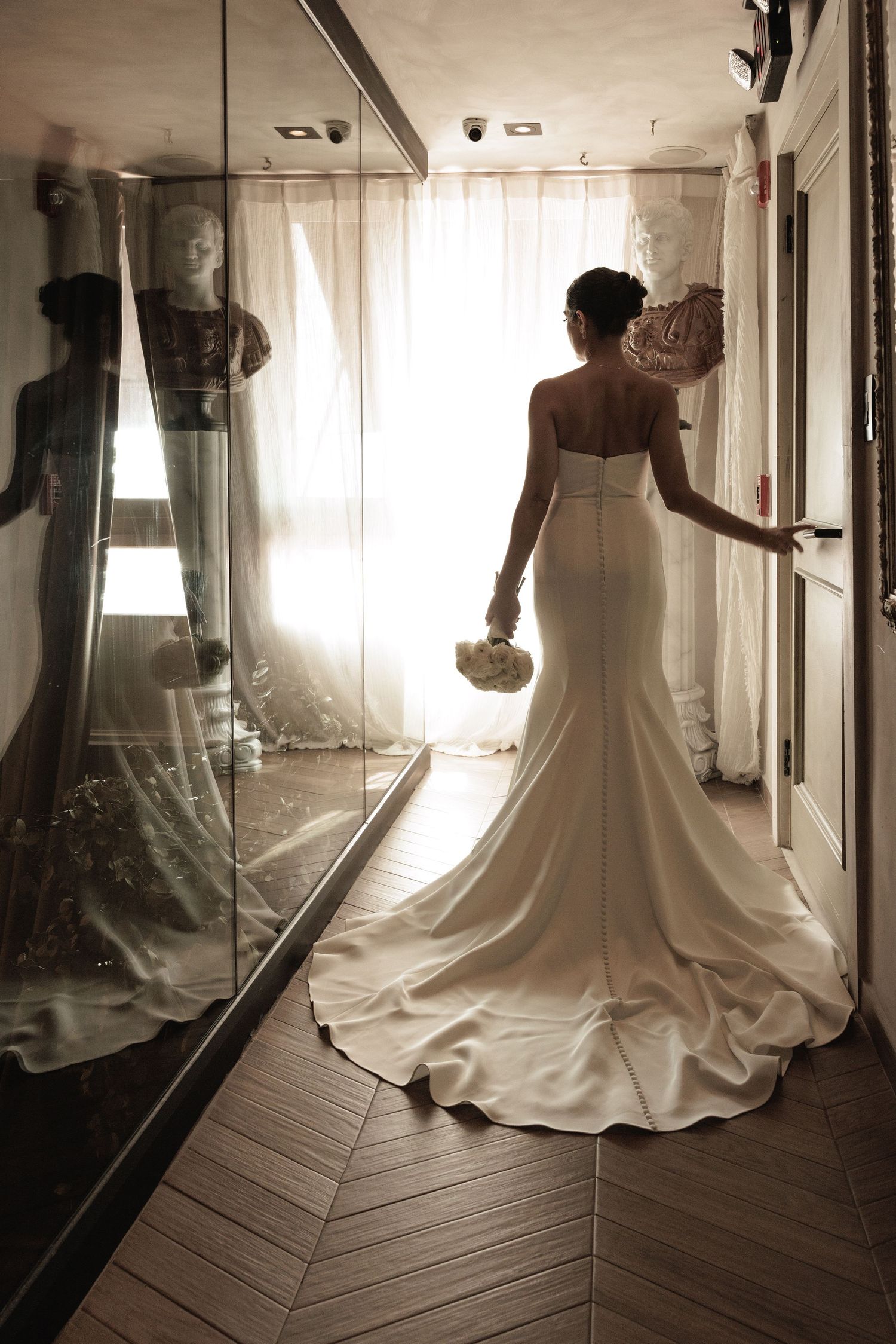 Dramatic silhouette of wedding dress against mirrored walls and wooden floors.