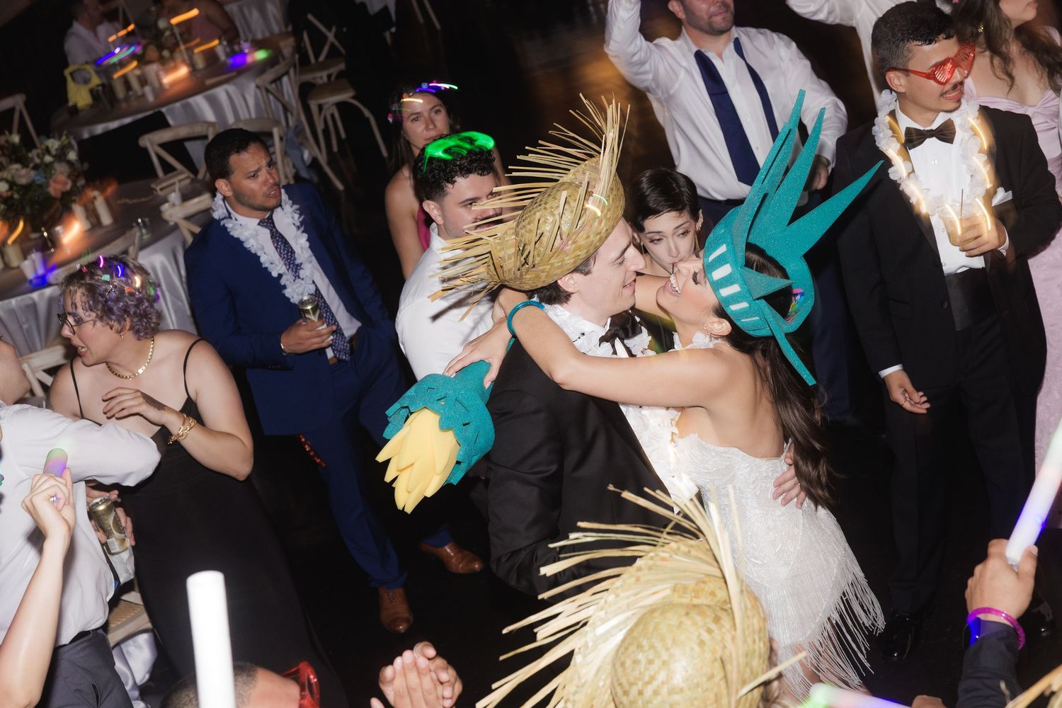 Party guests dance and celebrate on a crowded dance floor at an elegant event with colorful lighting.
