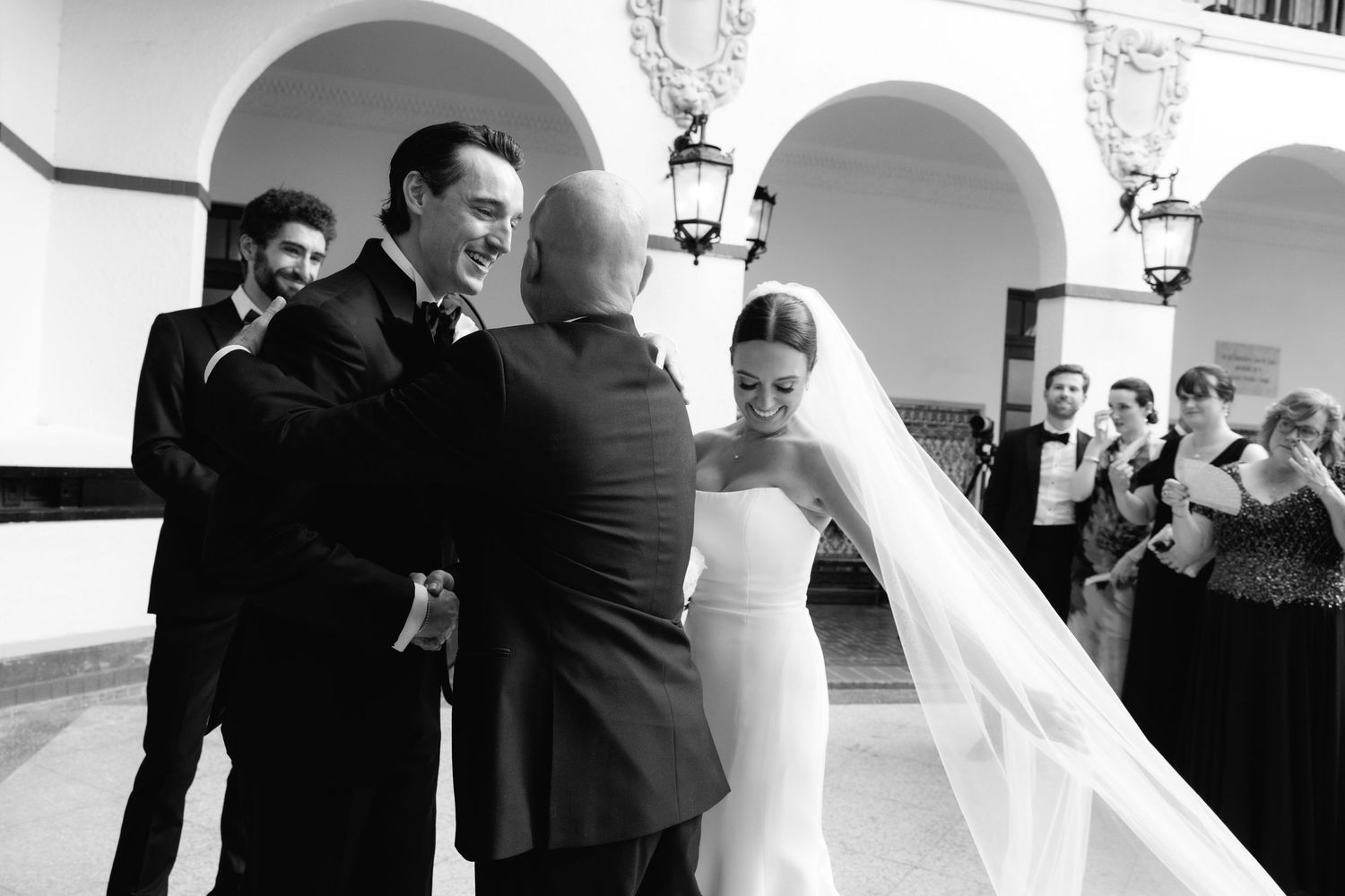 Black and white panoramic photo shows tender moments between wedding party members at an elegant venue.