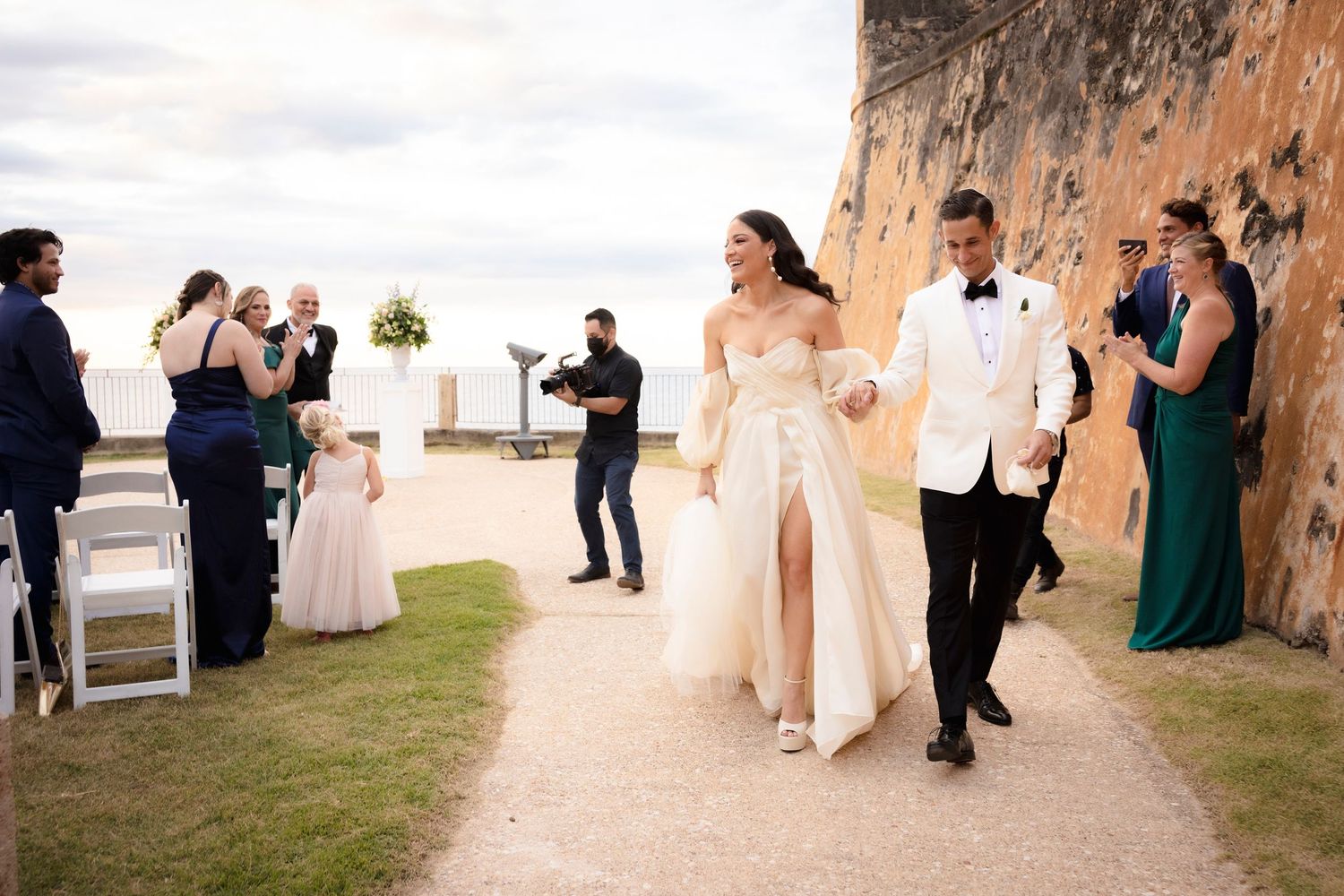 Wedding party and guests gathered outside historic stone fortress for celebration.