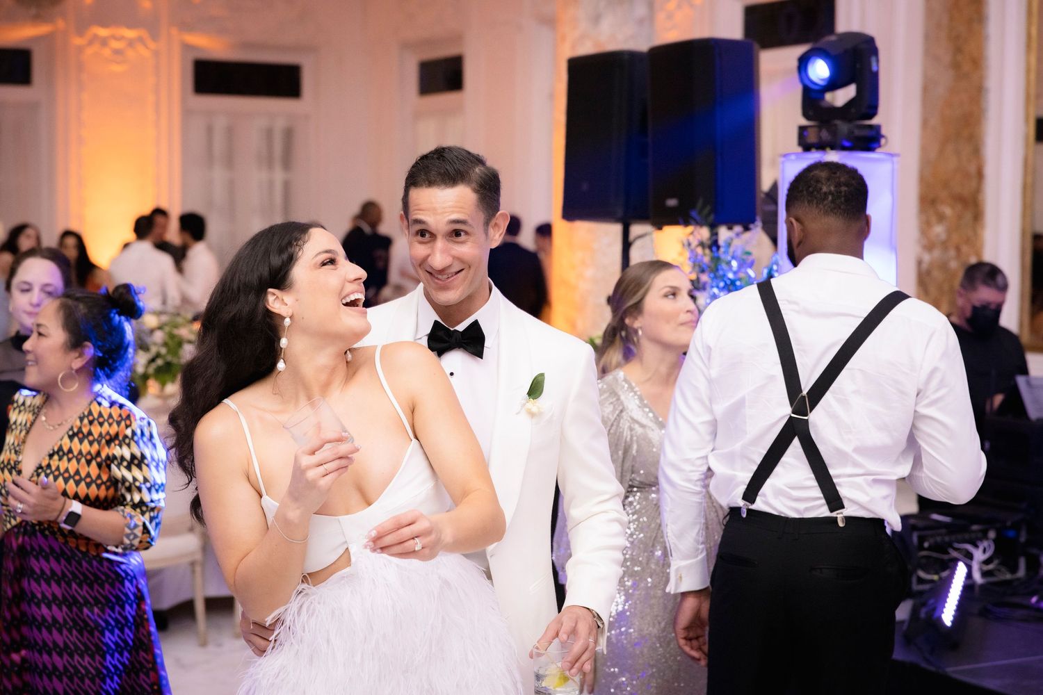 Wedding attendees dance and celebrate on a ballroom dance floor at a reception with warm lighting and elegant decor.