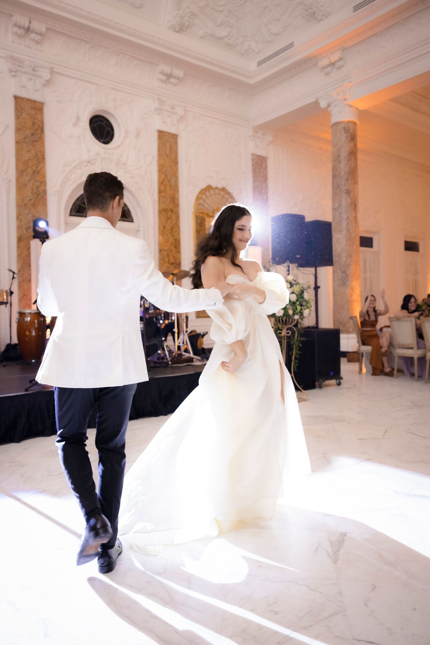 A wedding couple performs a graceful twirling dance sequence in a grand white ballroom.