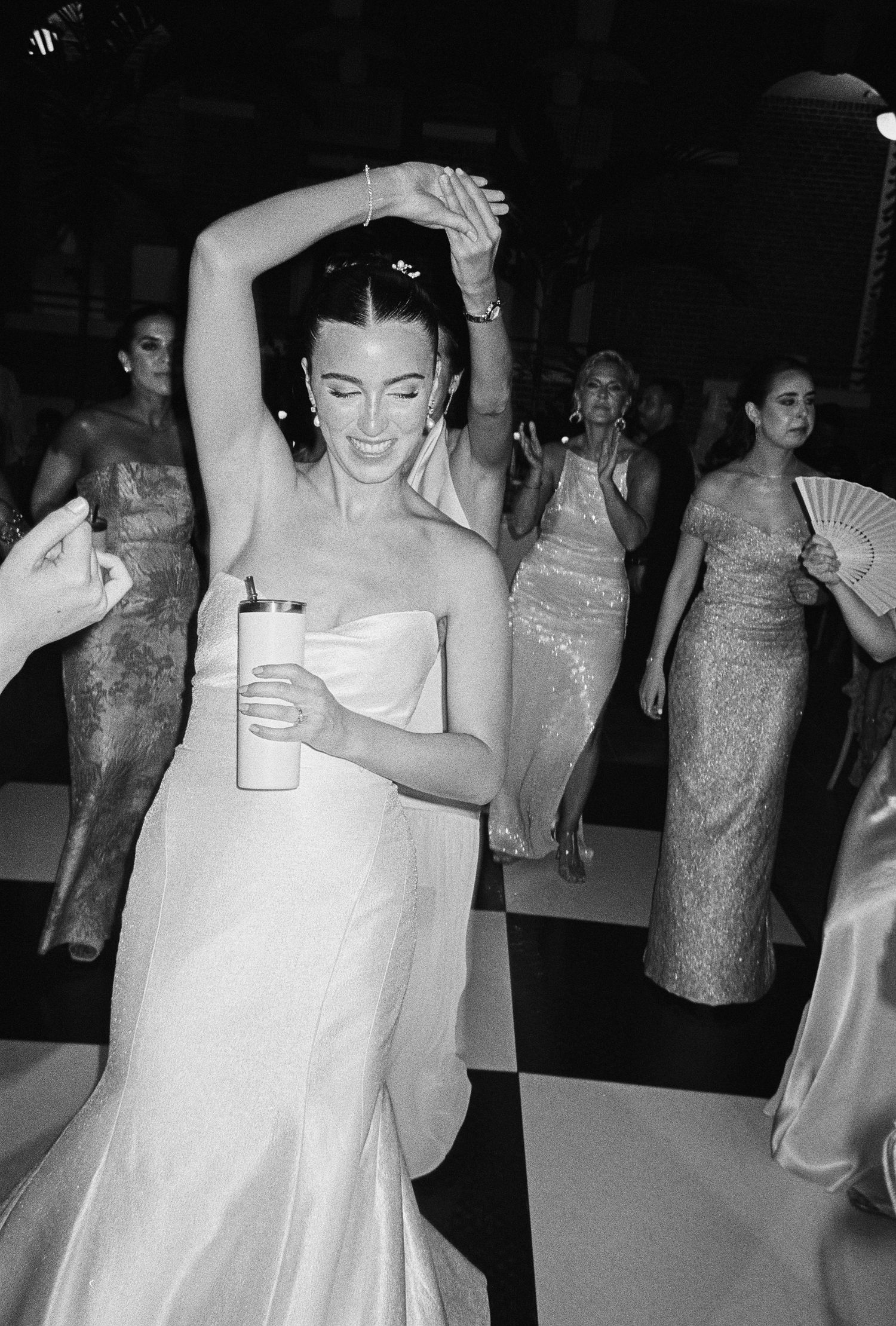Bride in strapless white gown dancing joyfully with bridesmaids in elegant dresses at a wedding reception.