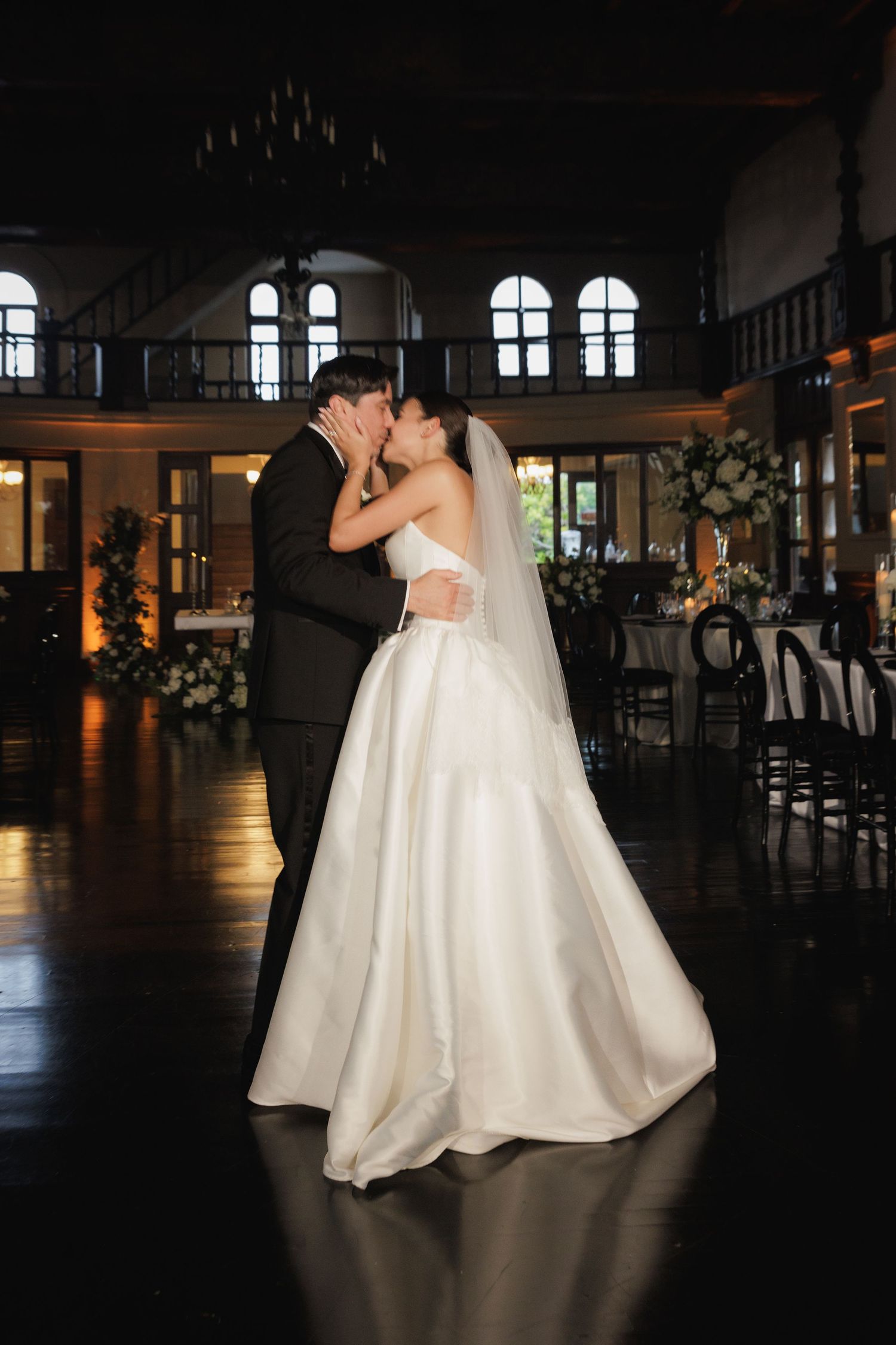 A romantic wedding dance silhouetted against arched windows in a grand ballroom with dramatic lighting.