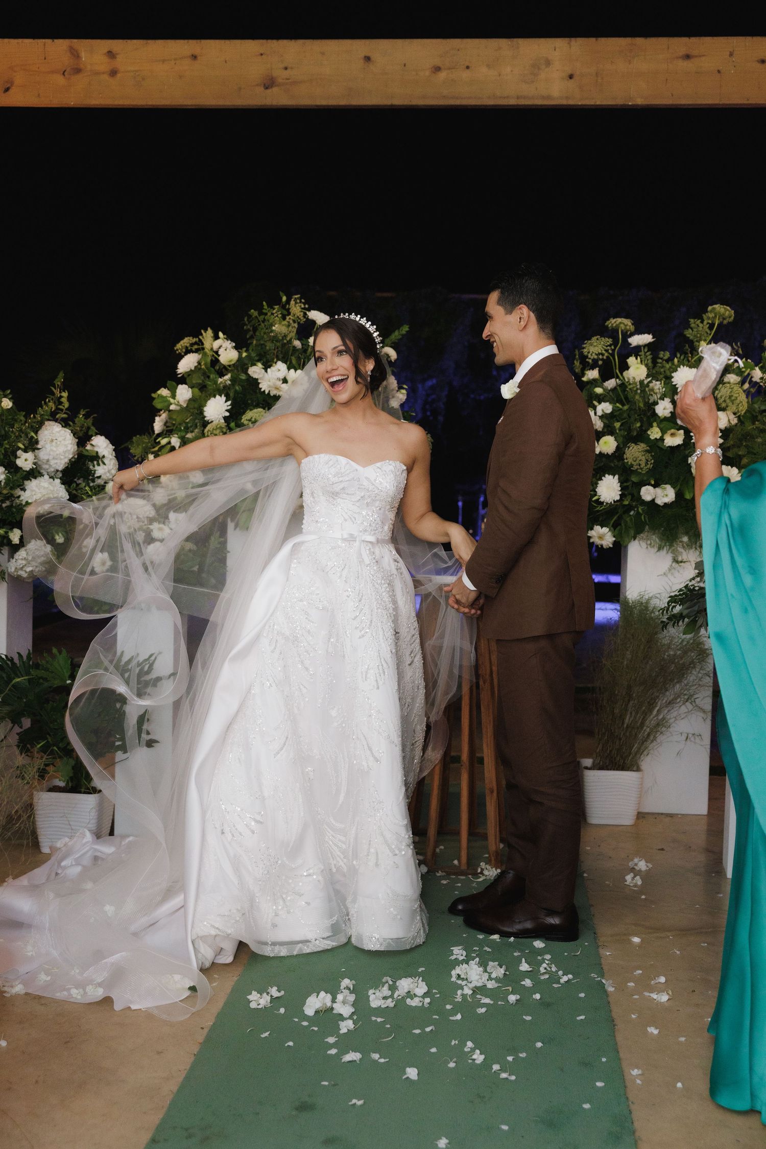 A joyful wedding celebration with flowing white dress and floral decorations on a green carpet.