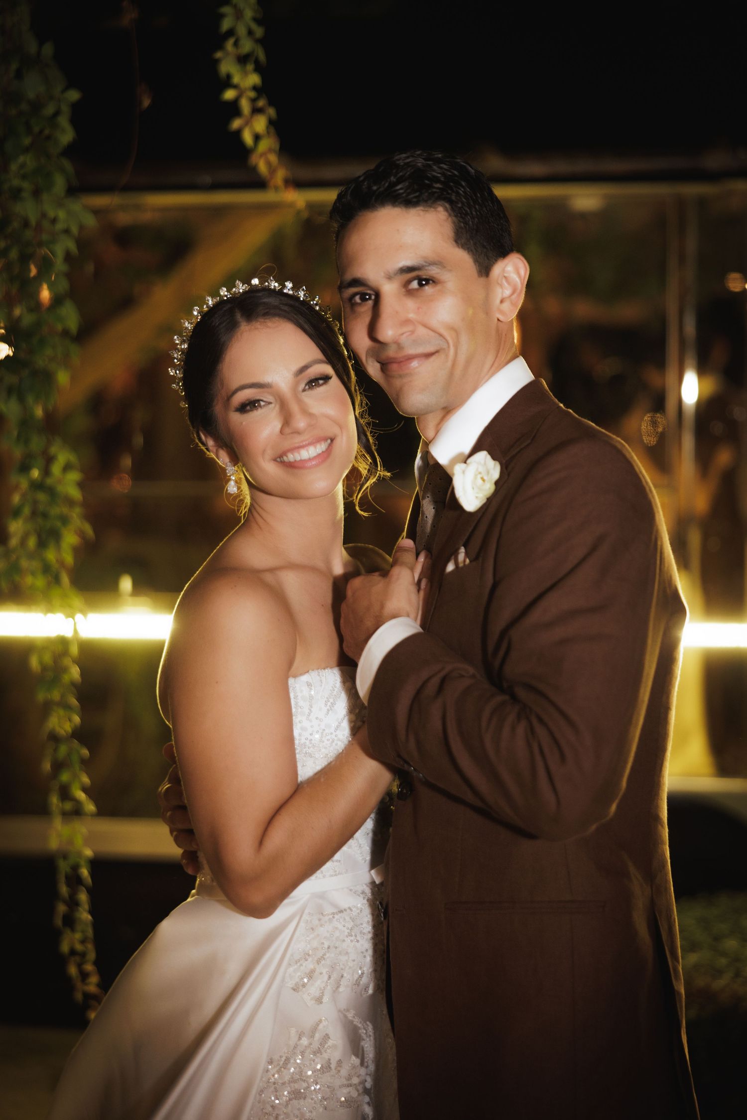 Bride in white gown and groom in brown suit share joyful moments during evening wedding reception.